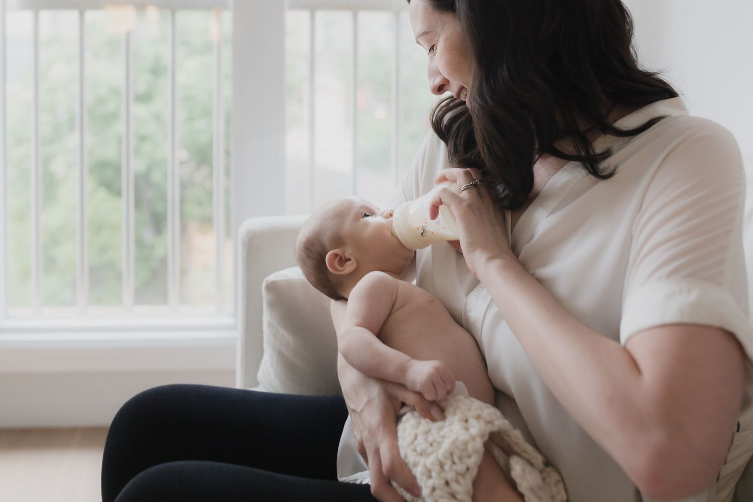Parent tenderly holding and interacting with newborn baby by window.