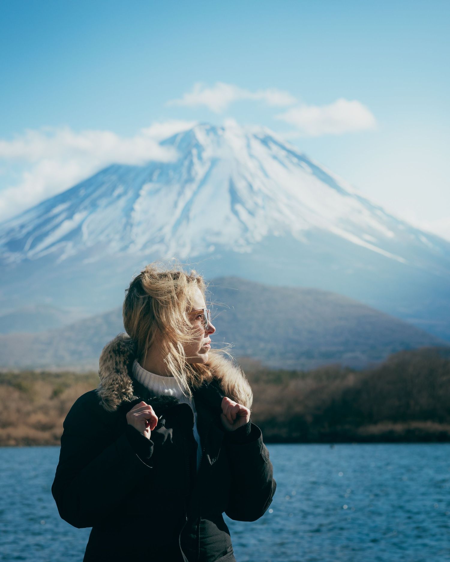 Scenic view of Mount Fuji with snow-capped peak rising above lake under blue sky.