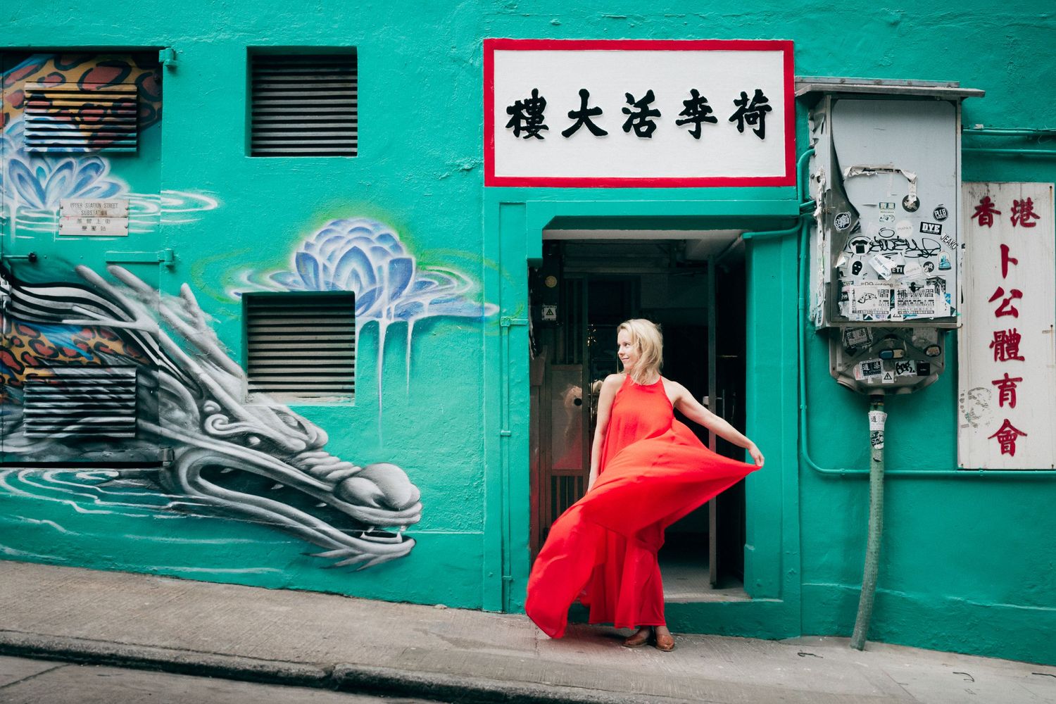 Woman in flowing red dress posing against turquoise wall with Chinese characters and street art.