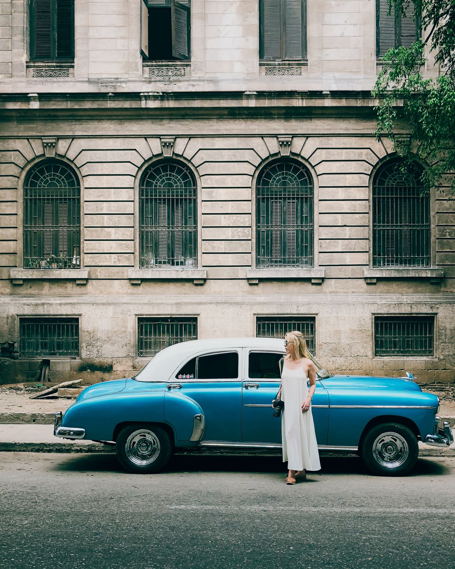 Classic blue vintage car parked in front of historic building with arched windows and shutters.
