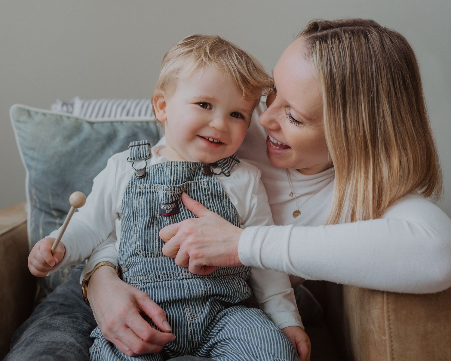 Parent and baby in striped outfit sharing tender moments on grey couch.