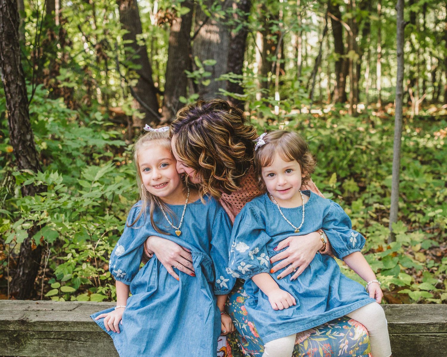 People wearing coordinated denim clothing sitting together on a bench in a wooded area.