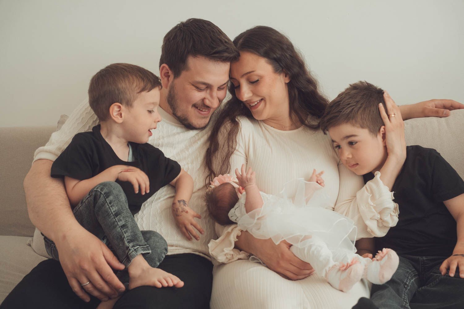 ein Familie Foto in einem Neugeborenen-Fotoshooting bei den Eltern zuhause. die Eltern mit den Geschwistern und dem neuen Baby umarmen sich