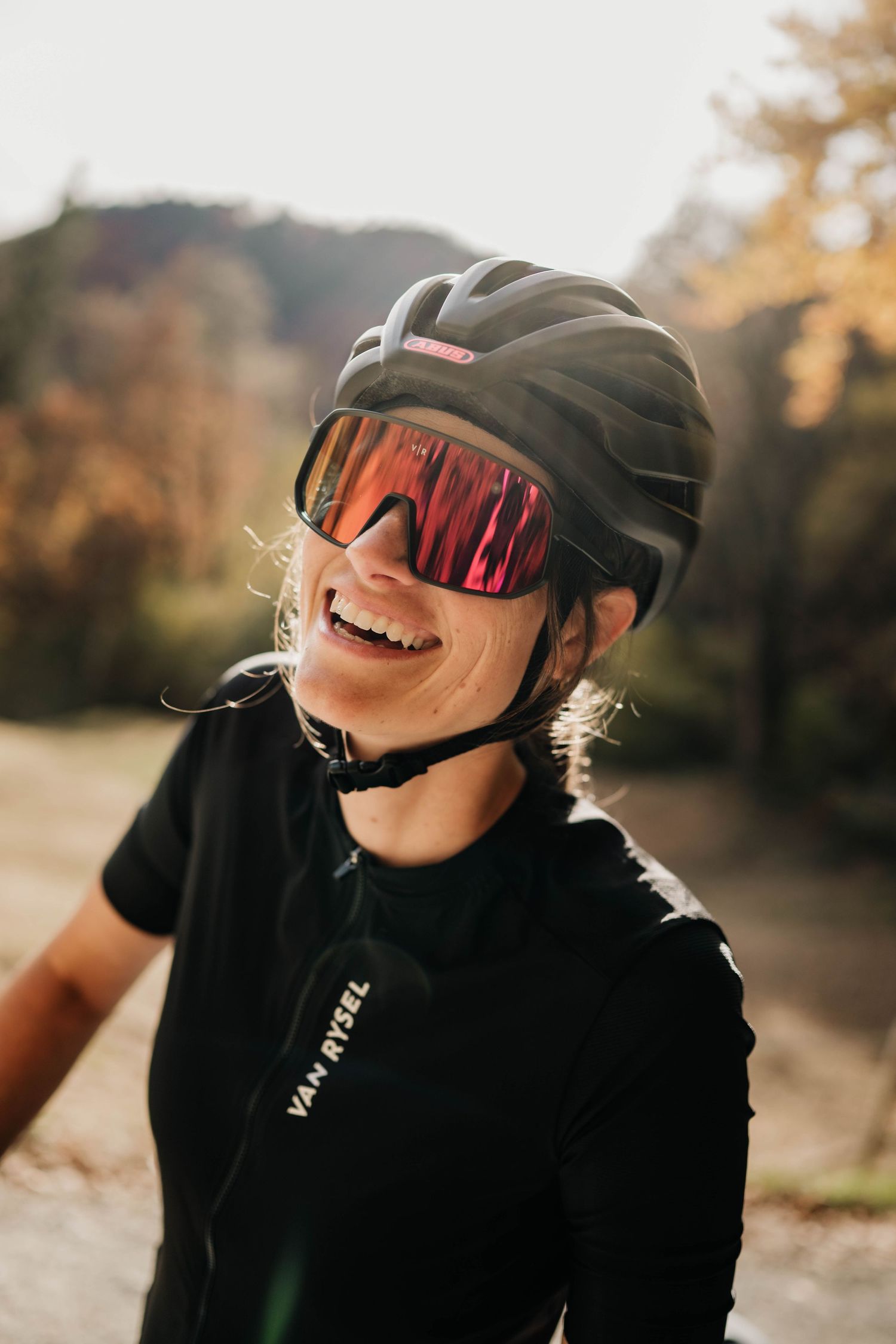 Cyclist wearing black helmet and sunglasses smiles joyfully during an autumn bike ride on a sunny day.