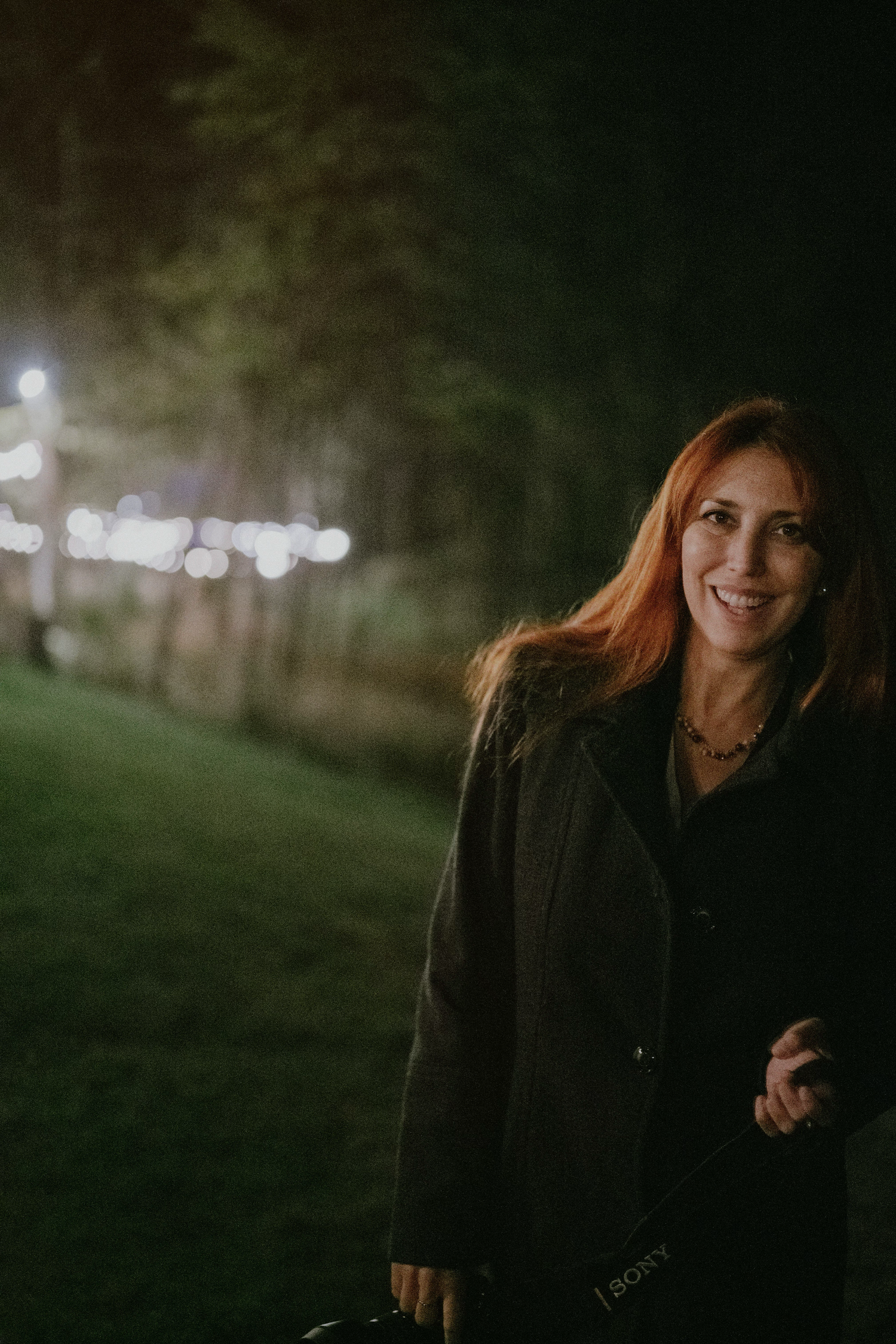 A person in dark clothing stands outdoors at night with a moody atmospheric lighting effect.