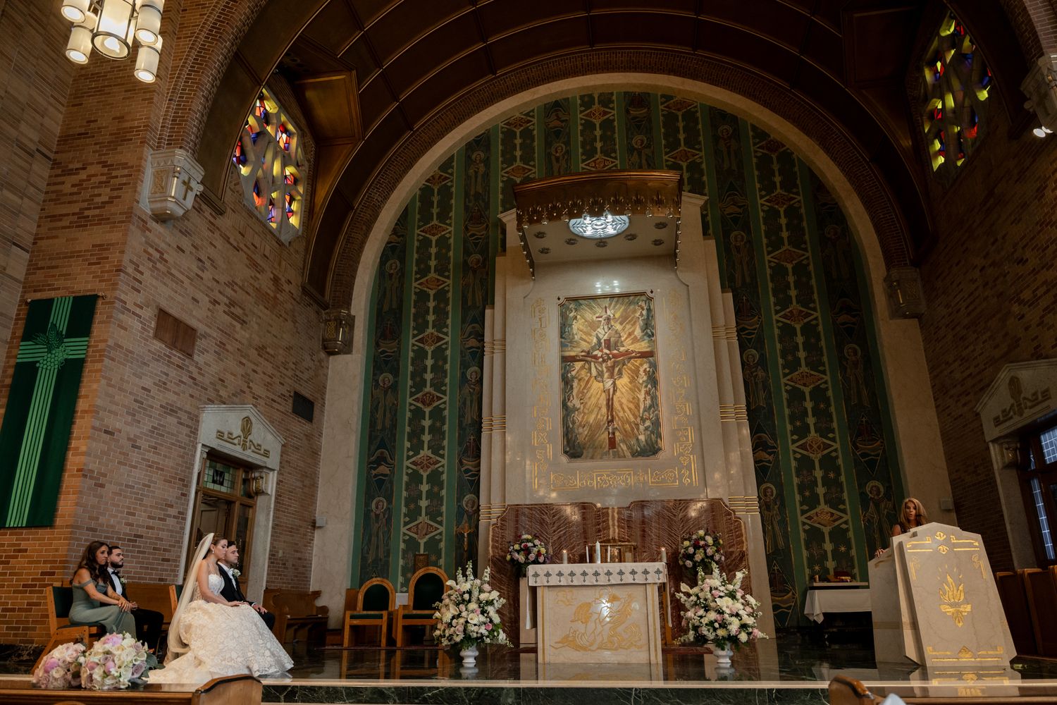 A wedding ceremony in a Catholic church with arched ceilings, stained glass windows, and ornate altar decorations.