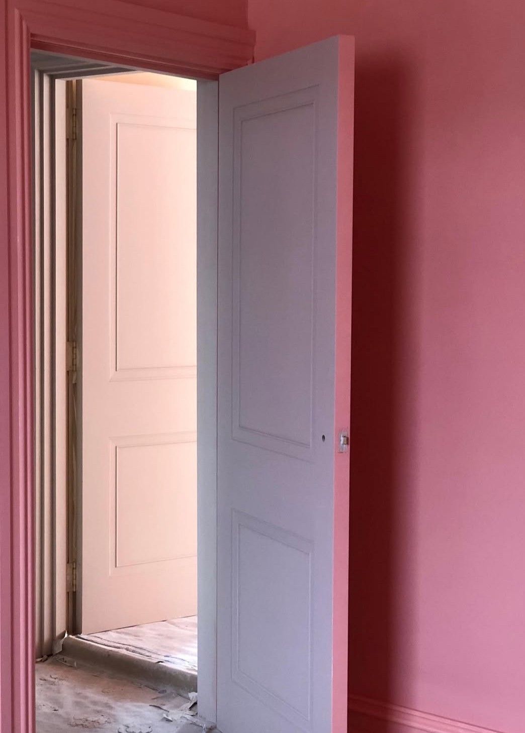 A white door opens to reveal a pink painted hallway with deep coral walls and soft natural lighting.