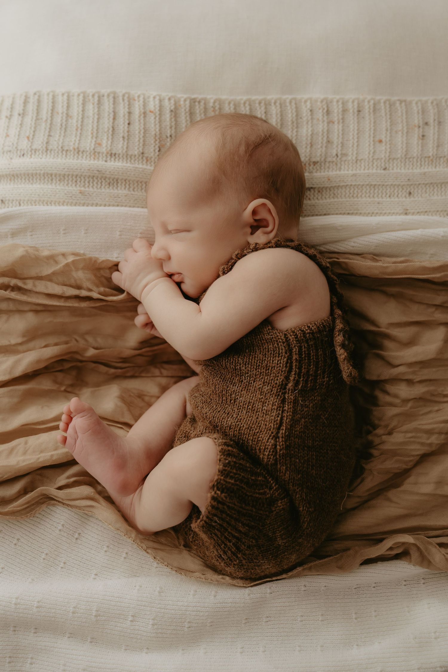 Sleeping newborn baby in a brown knit romper on soft linen during a natural newborn photography session in Perth