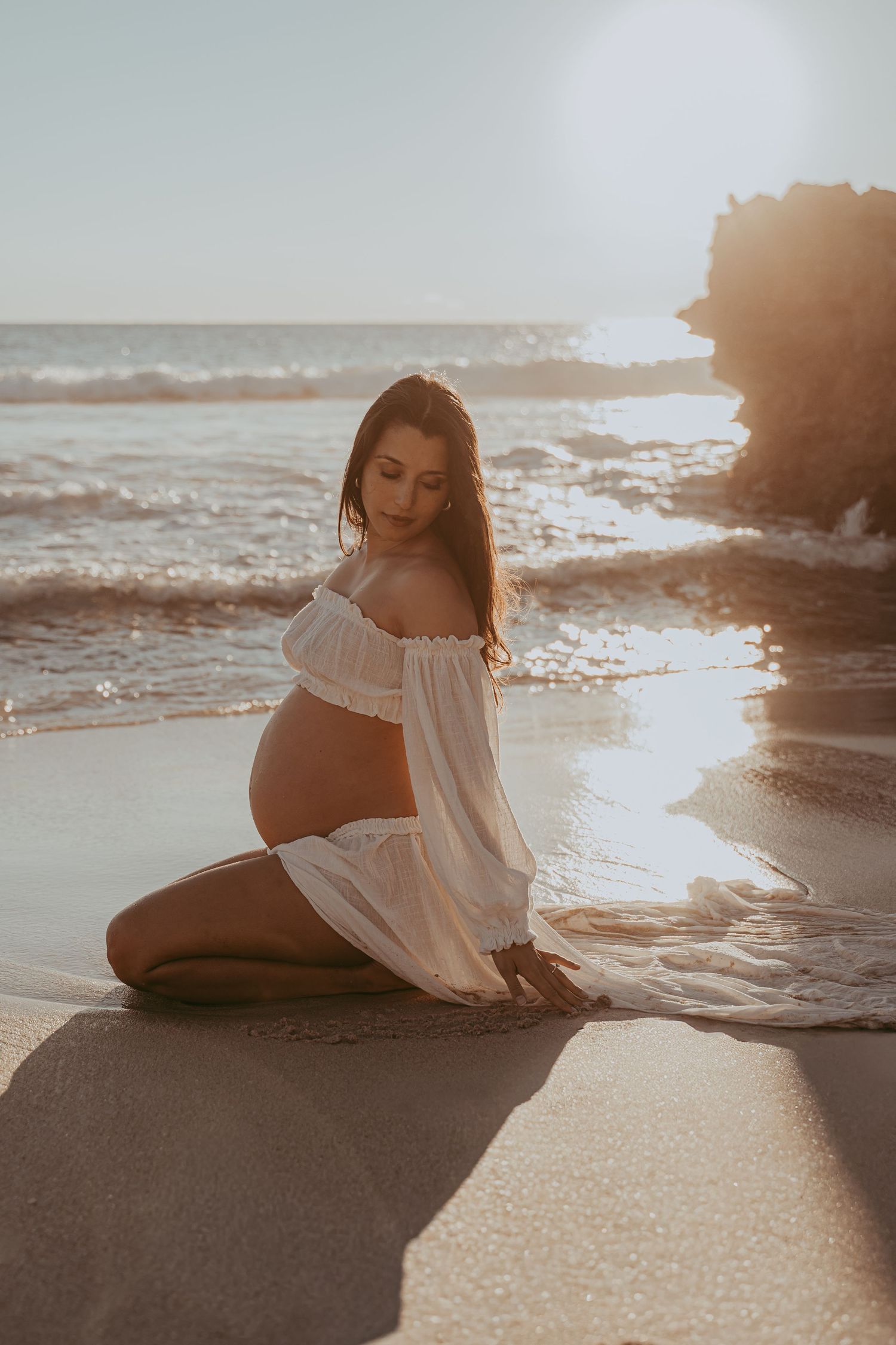 Expectant mother wearing a white dress during a golden hour beach maternity photography session in Perth.