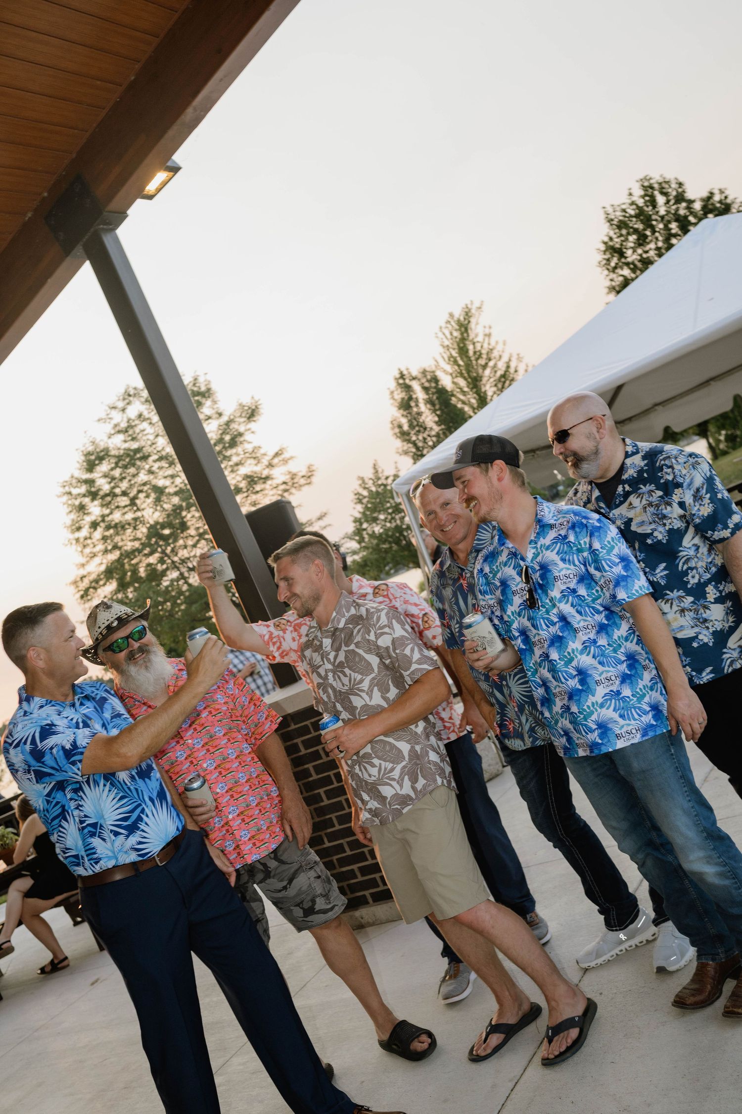 Group of men in colorful Hawaiian shirts celebrating at outdoor wedding reception.
