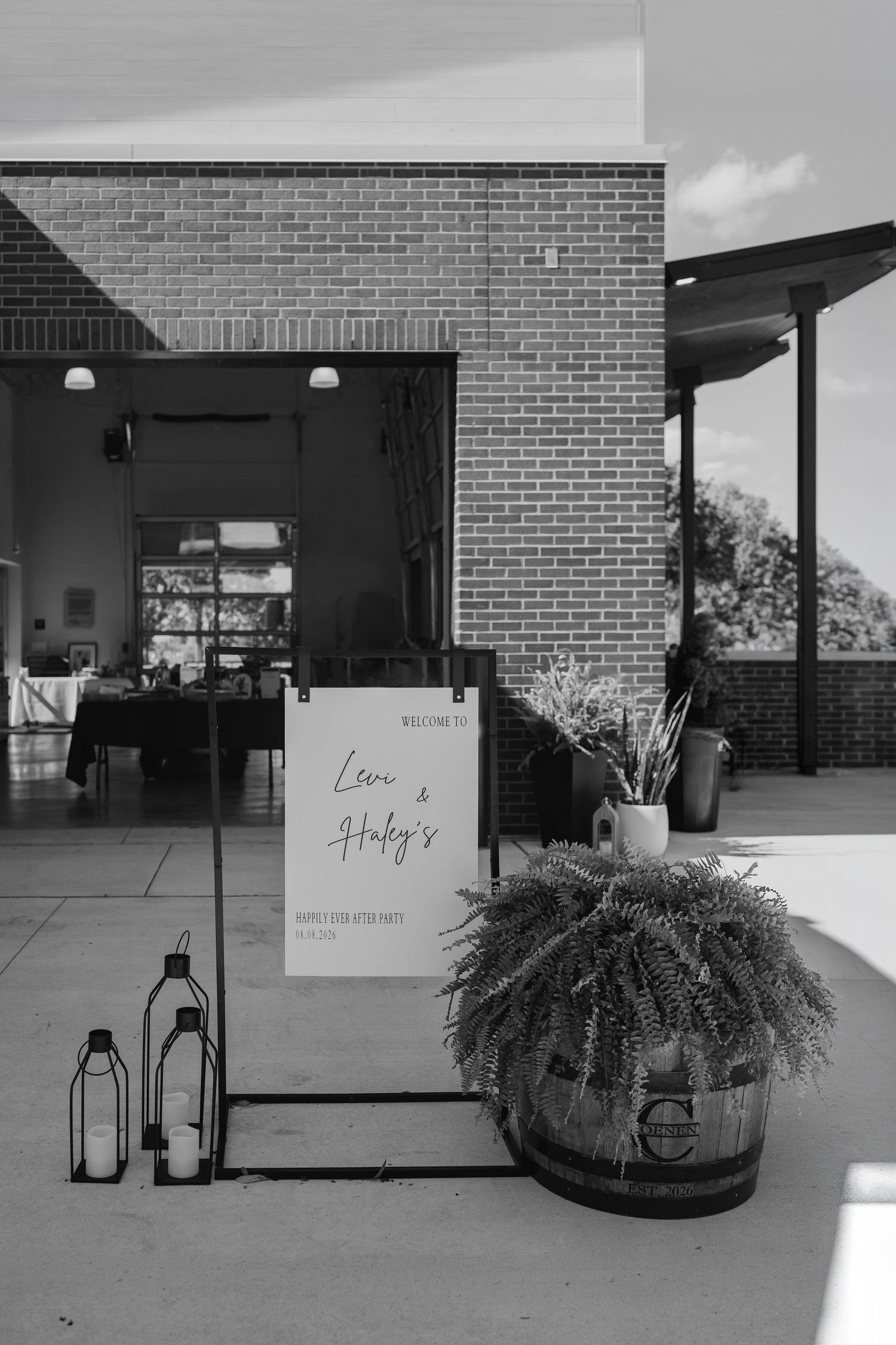 Black and white wedding welcome sign for Levi and Huby displayed outside on a barrel with lanterns.
