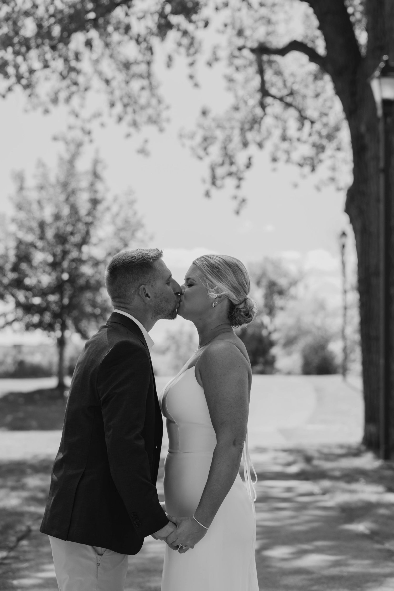 Black and white photo of newlyweds sharing a tender kiss outdoors on their wedding day.
