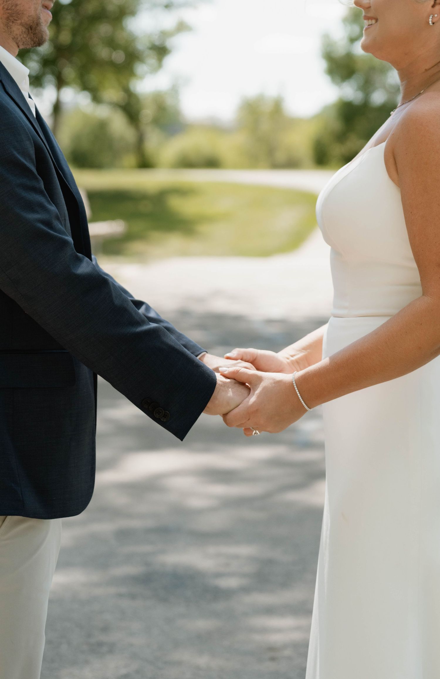 Close-up of bride and groom holding hands on a sunny path on their wedding day.
