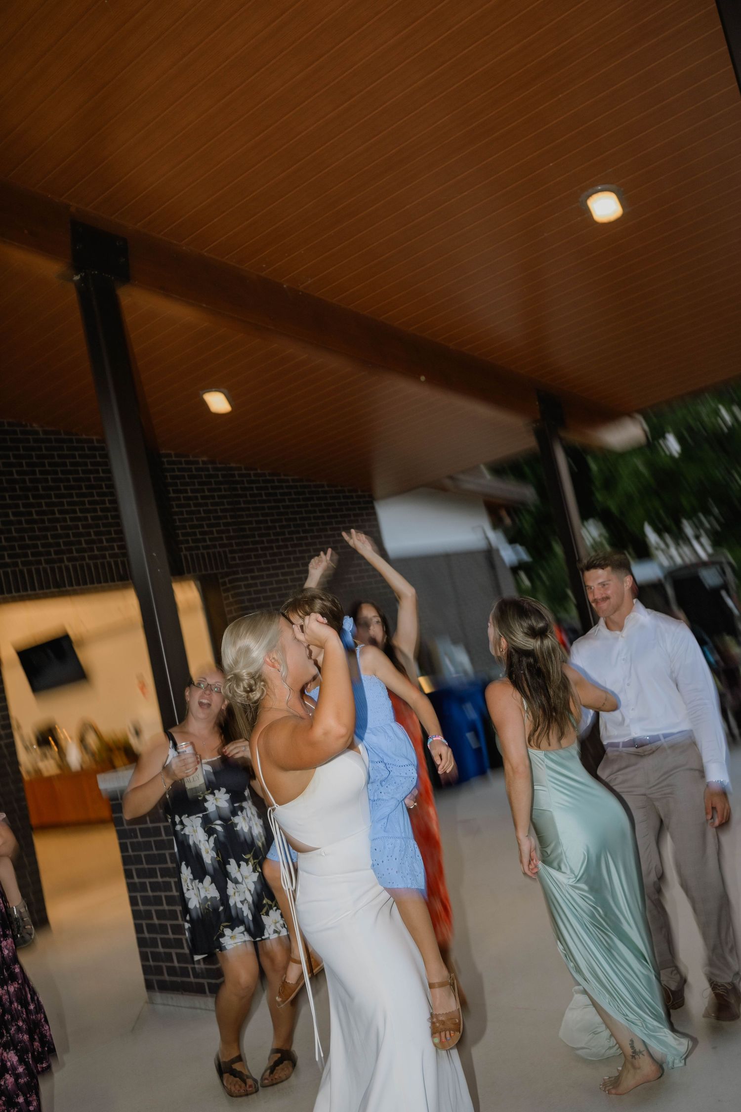 Bride and guests dance under wooden pavilion ceiling at lively indoor-outdoor wedding reception.