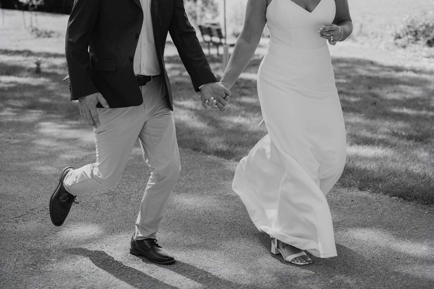 Black and white photo of bride and groom playfully running hand in hand on their wedding day.