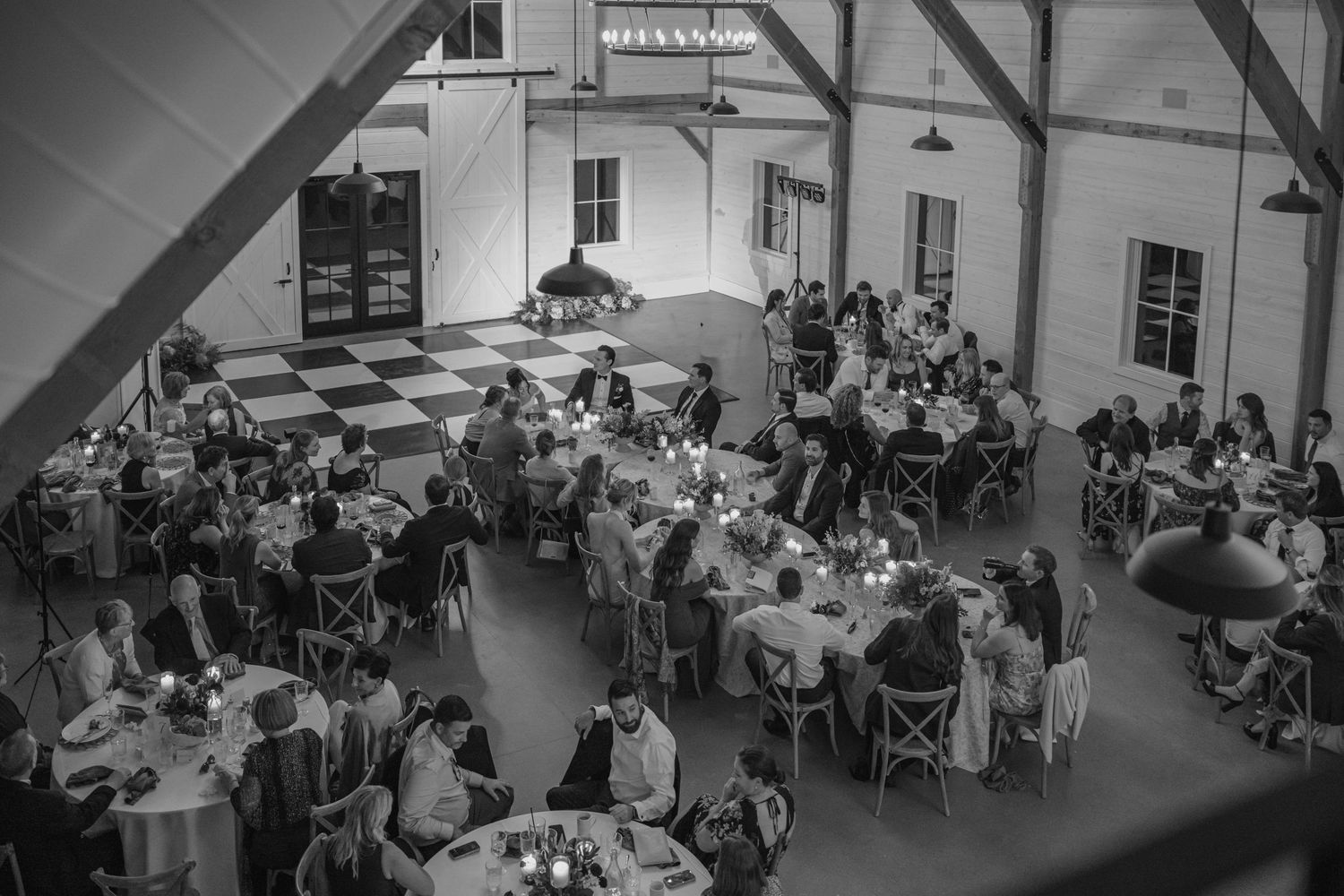 Black and white aerial view of elegant wedding reception with round tables and guests dining in a rustic barn venue.