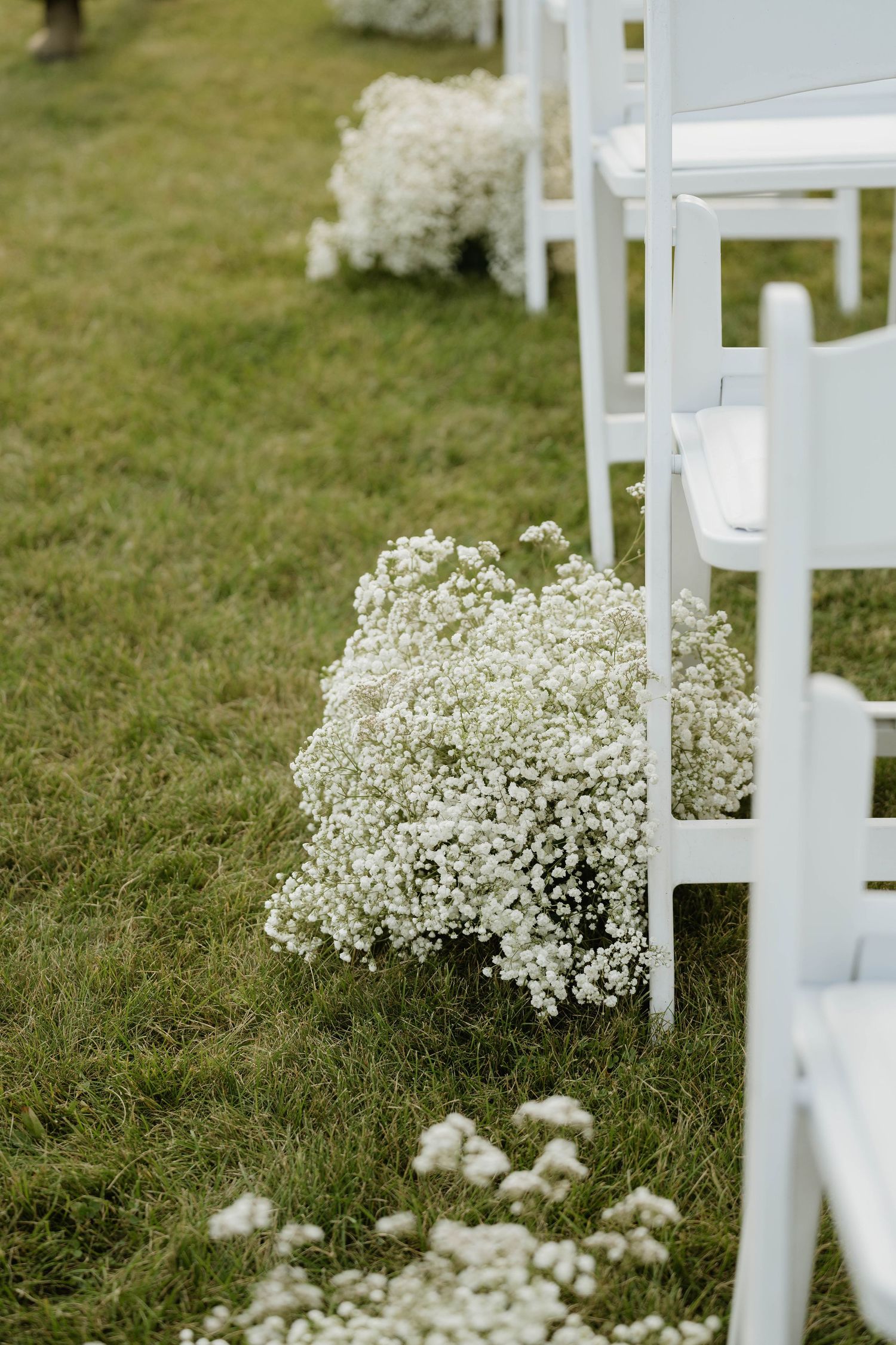 White baby's breath flower arrangements lining the aisle of an outdoor wedding ceremony on grass.