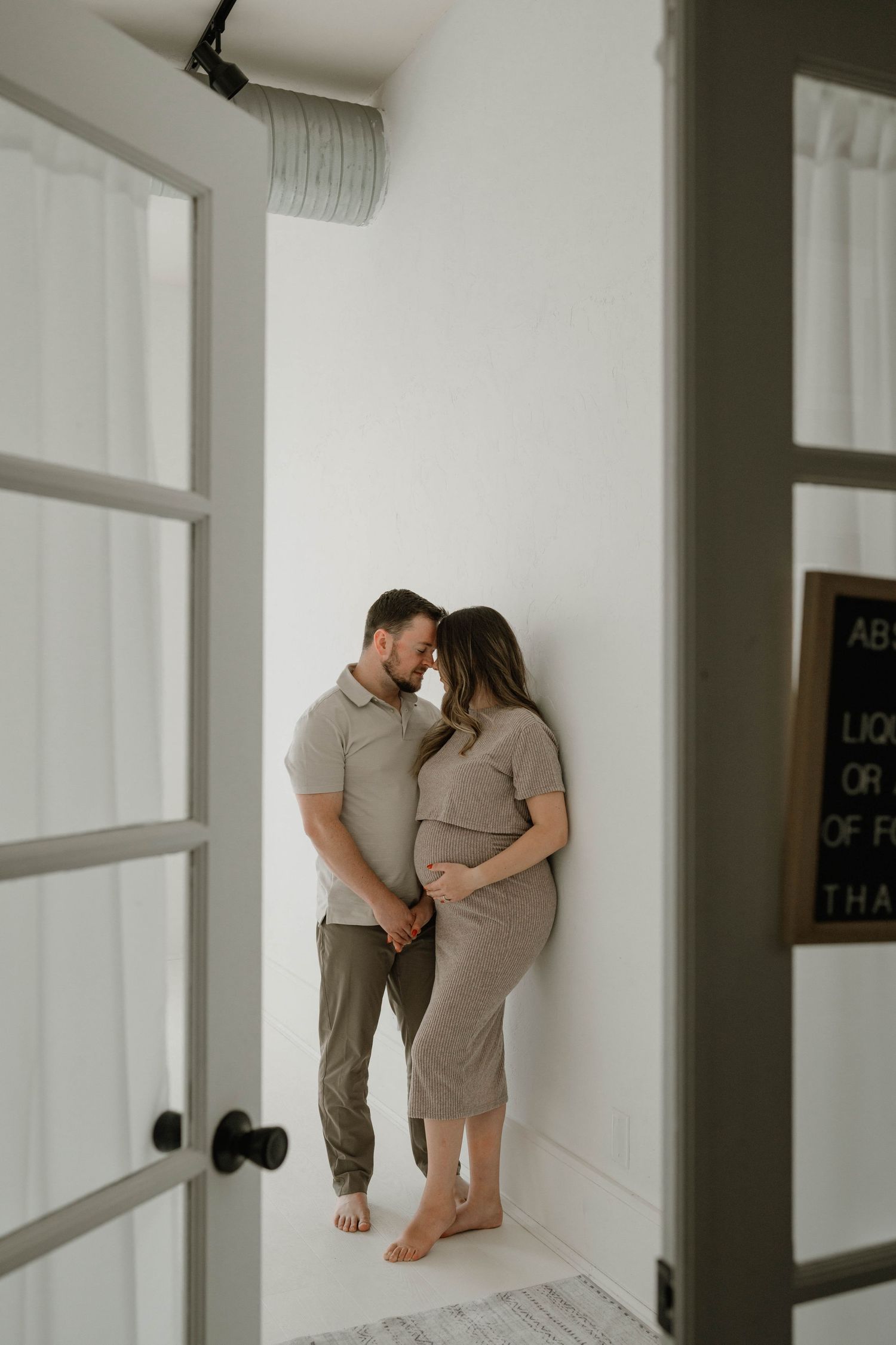 A couple shares an intimate moment, touching foreheads while the woman shows her pregnant belly.