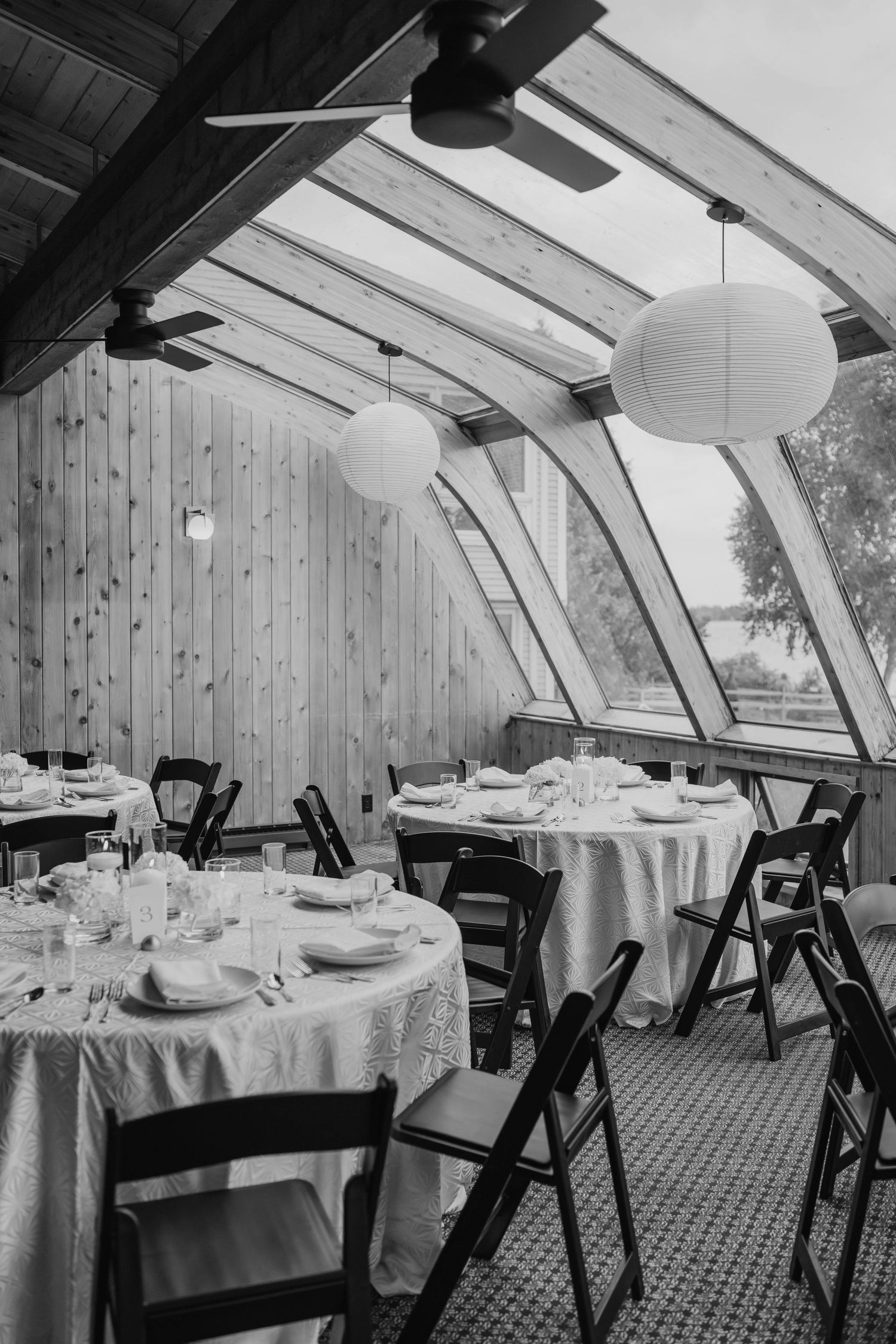 Elegant wedding reception room with arched wood ceiling, round tables, and globe pendant lights.