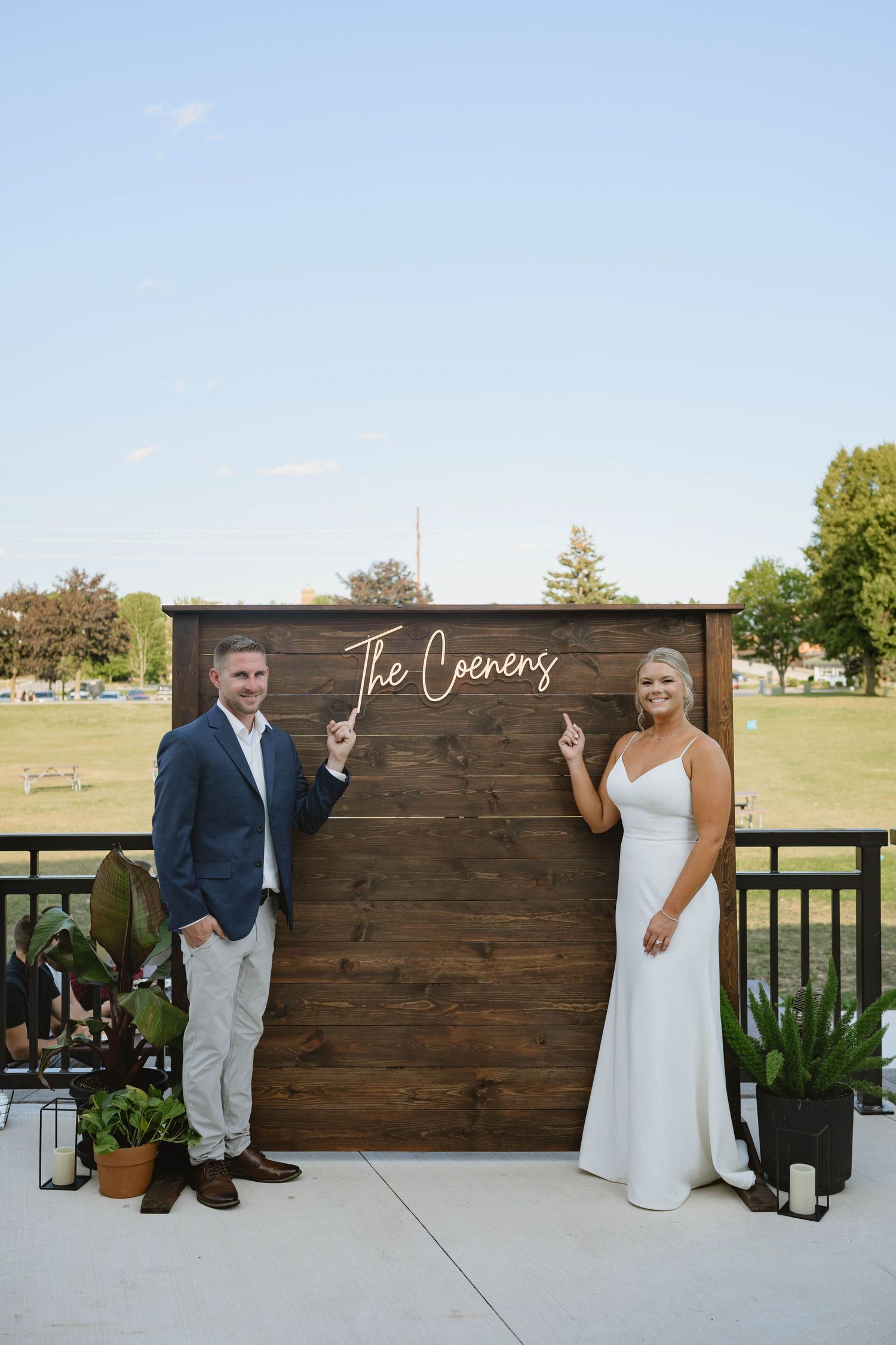 Newlyweds posing proudly in front of a wooden sign reading The Coenens at their wedding.