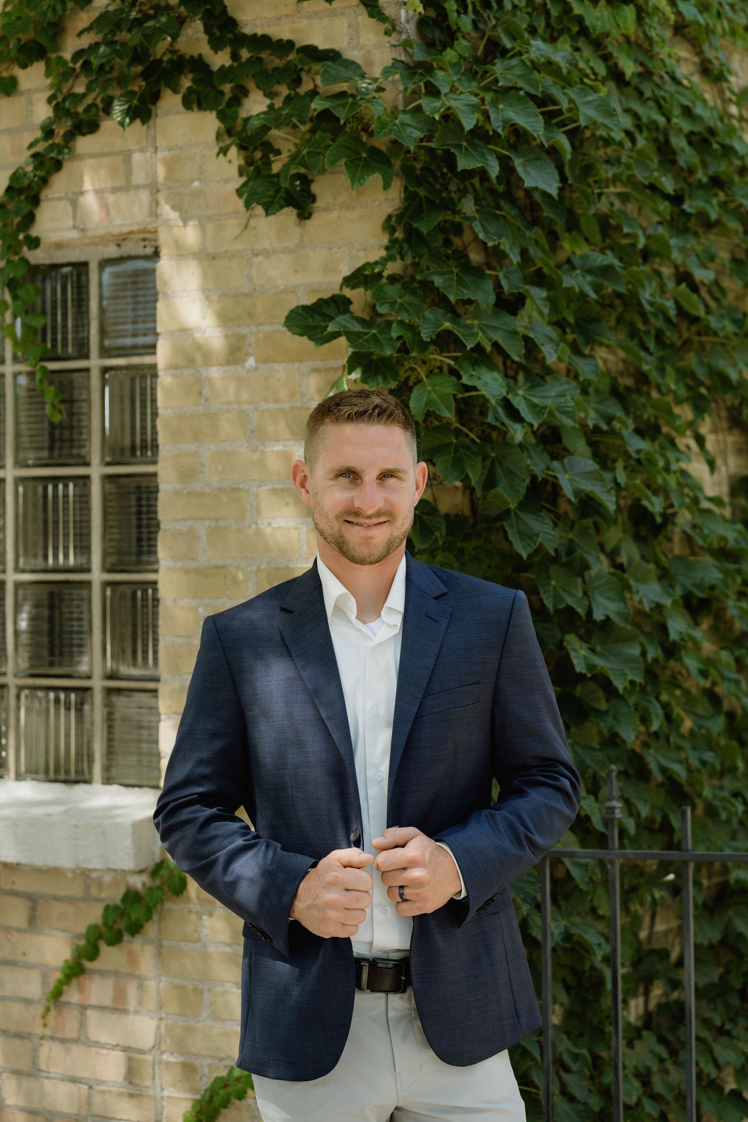 Groom in navy blazer smiling in front of ivy-covered brick building.