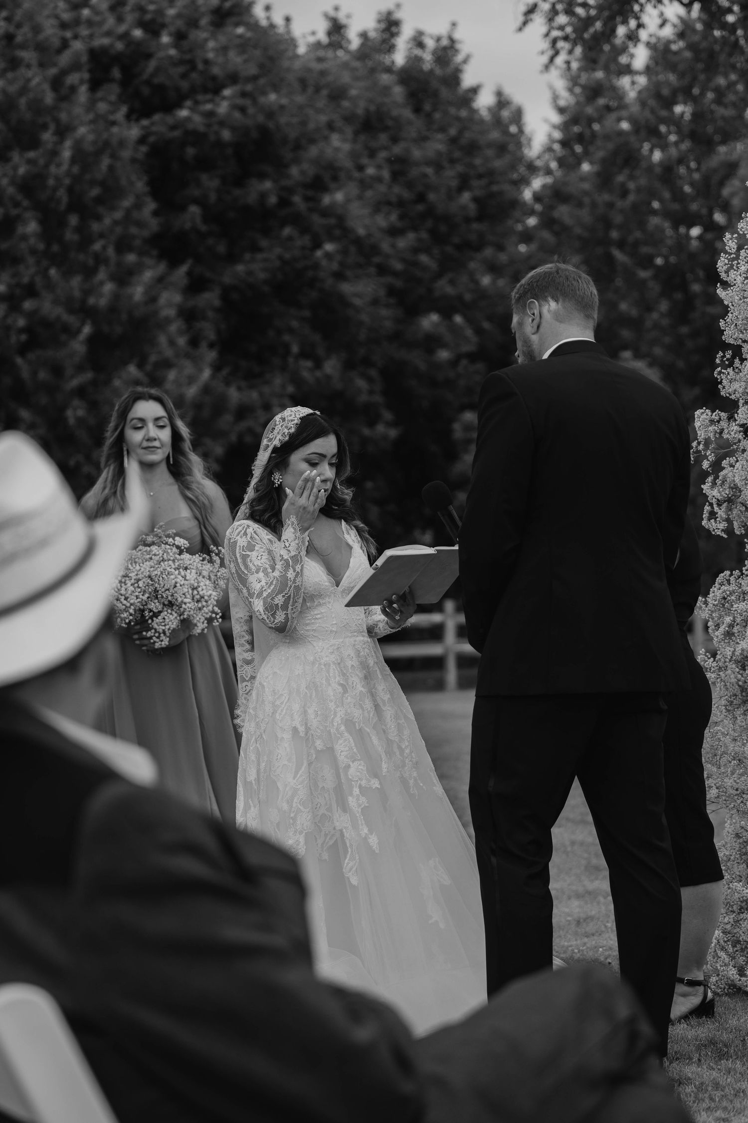 Black and white photo of emotional bride reading vows to groom at outdoor wedding ceremony.
