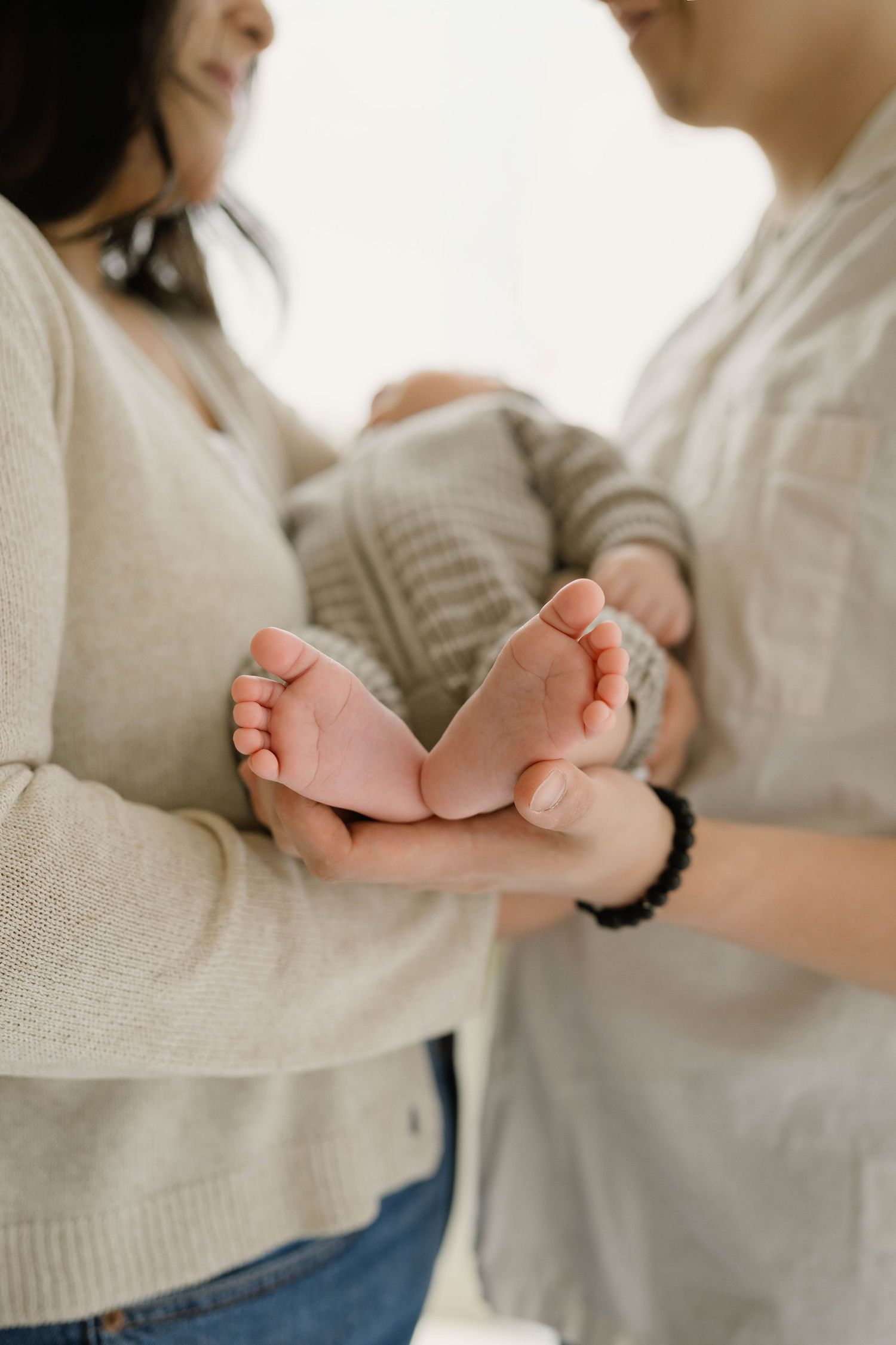 Parents tenderly cradle their newborns tiny feet together in a bright and airy indoor setting.