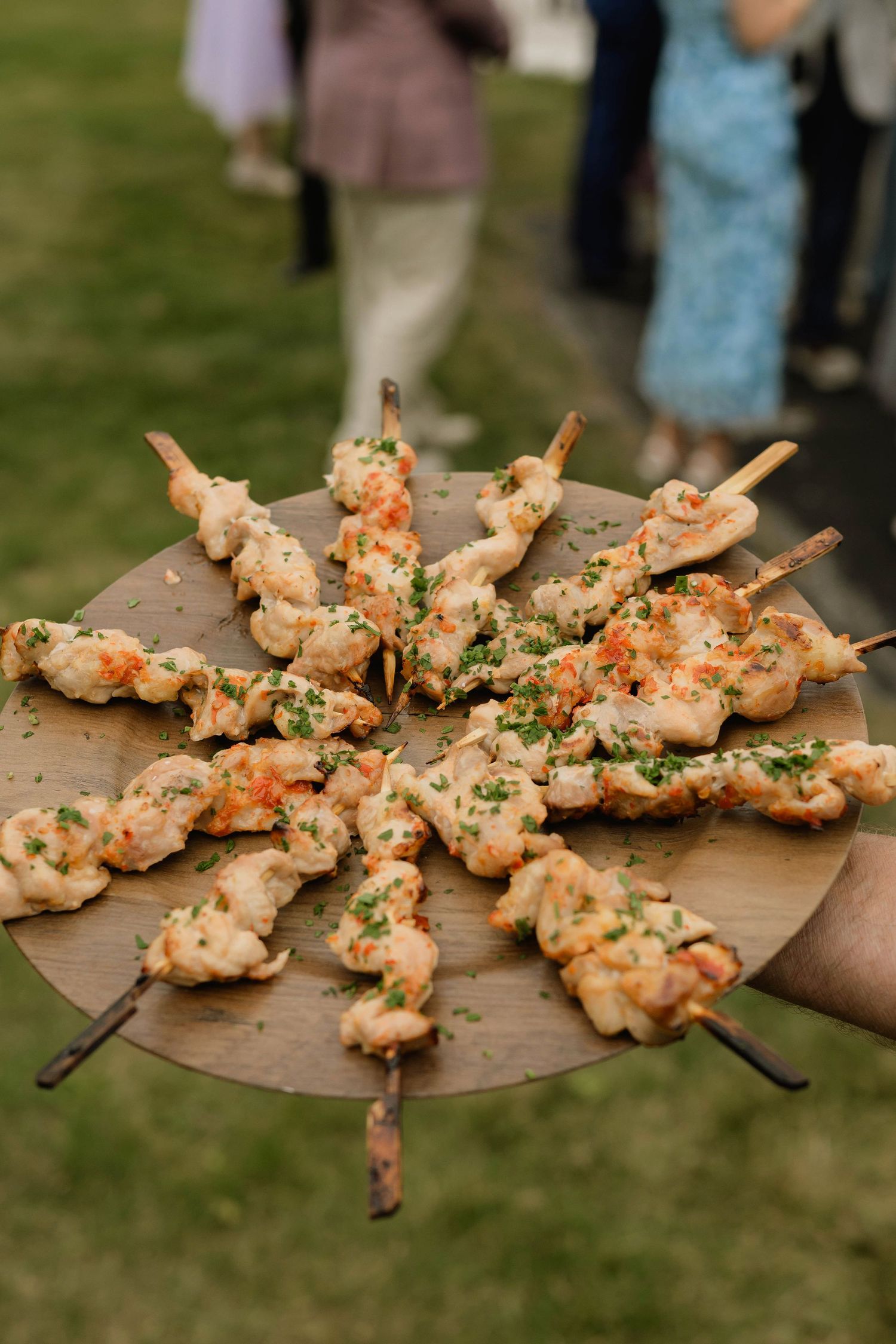 Catered wedding appetizers of grilled shrimp skewers with herbs served on a round wooden board.