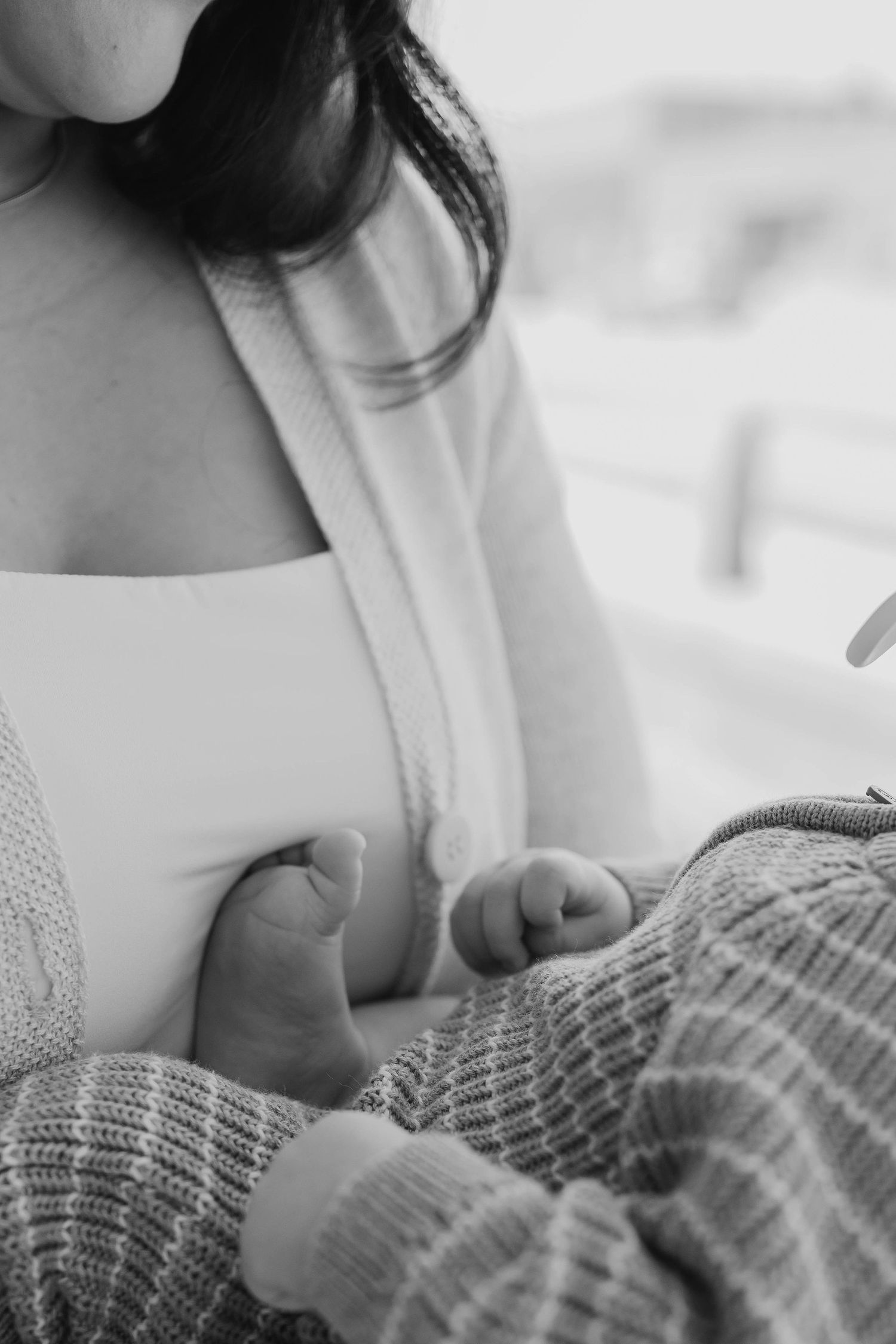 Black and white close-up of a mother breastfeeding her newborn baby wrapped in a knit cardigan.