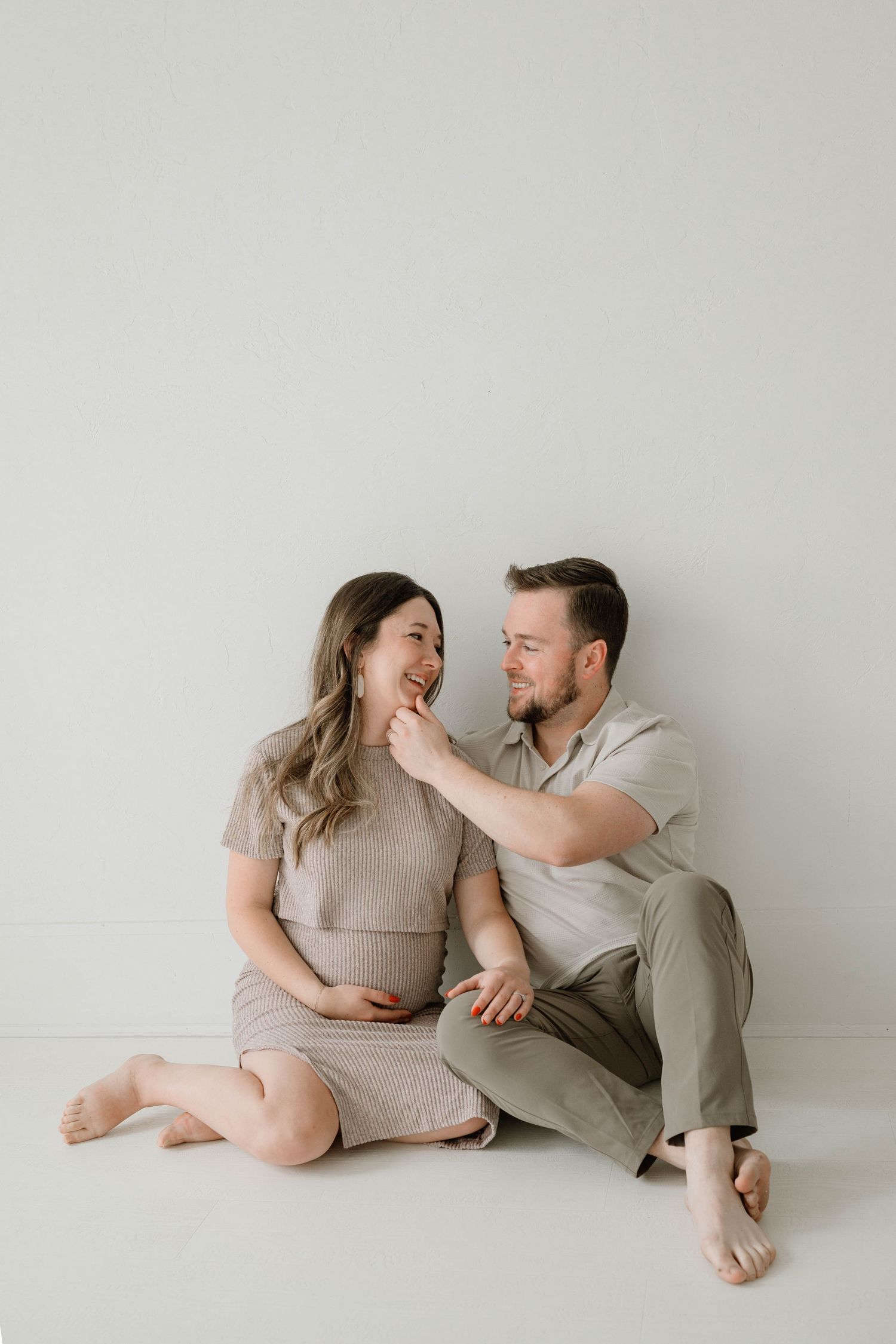 Couple sitting on floor, man tenderly touching pregnant woman's face in white studio.