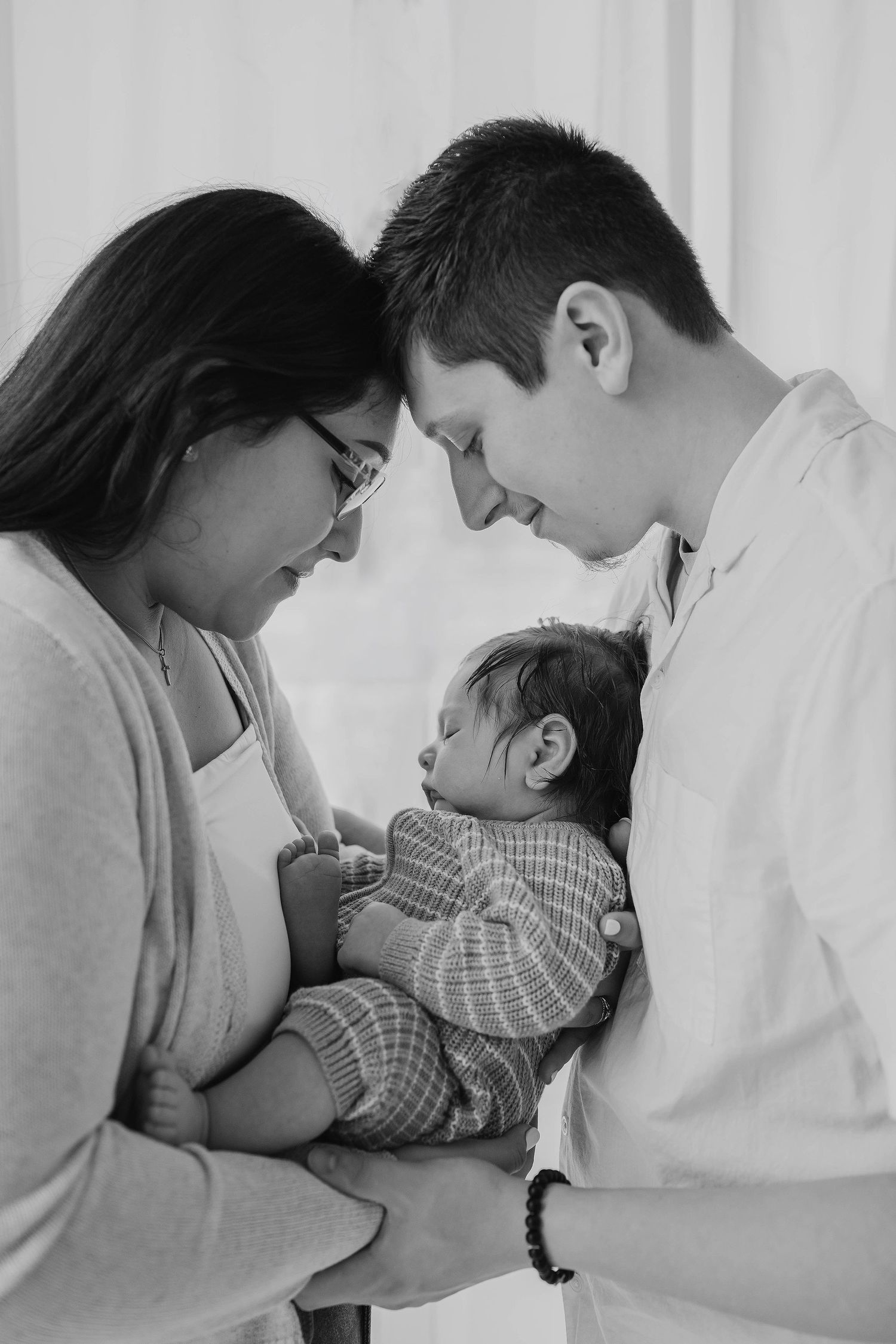 Black and white photo of new parents lovingly cradling their sleeping newborn baby together.
