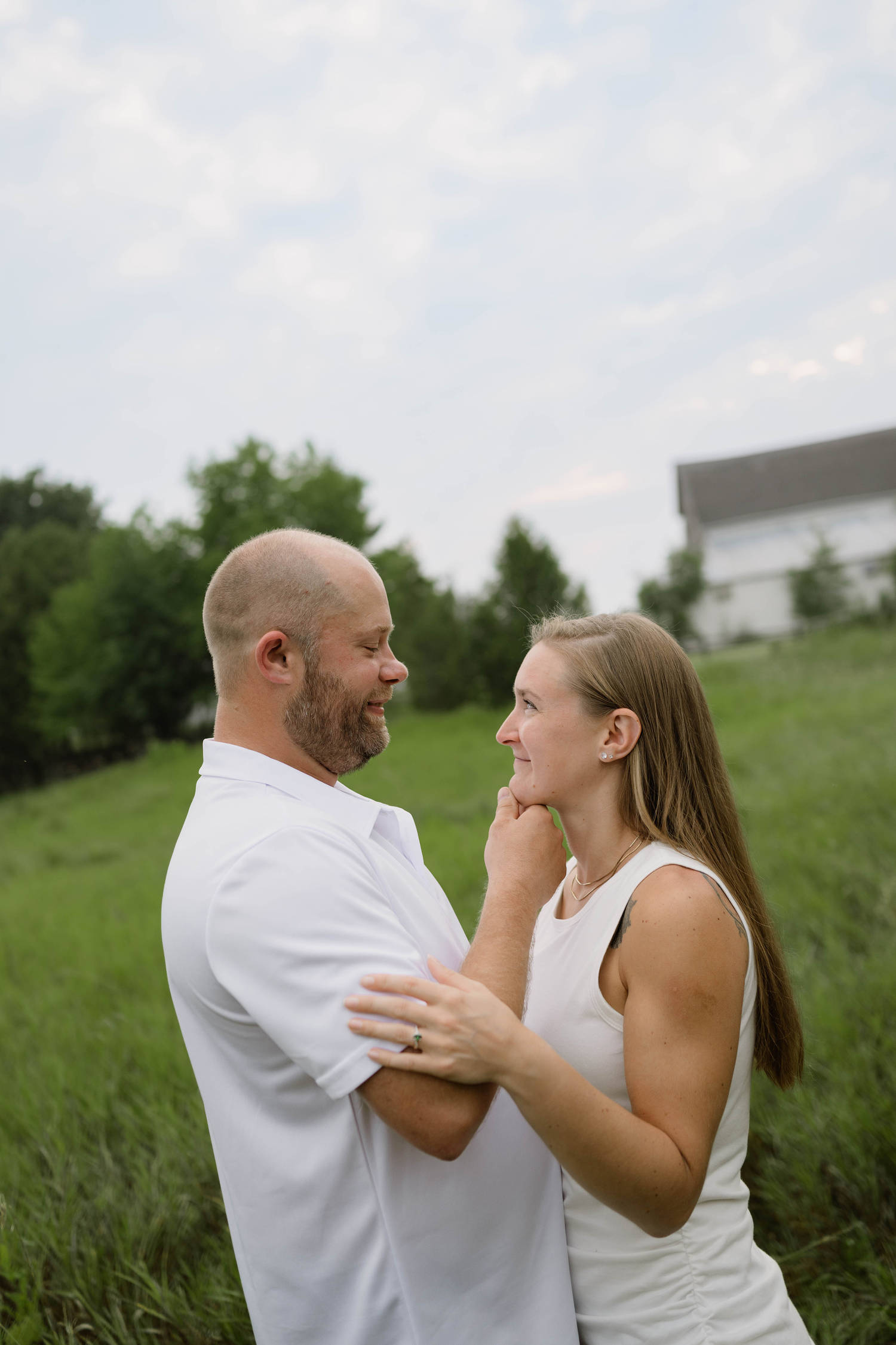 A couple gazes lovingly at each other while standing in a lush green field outdoors.