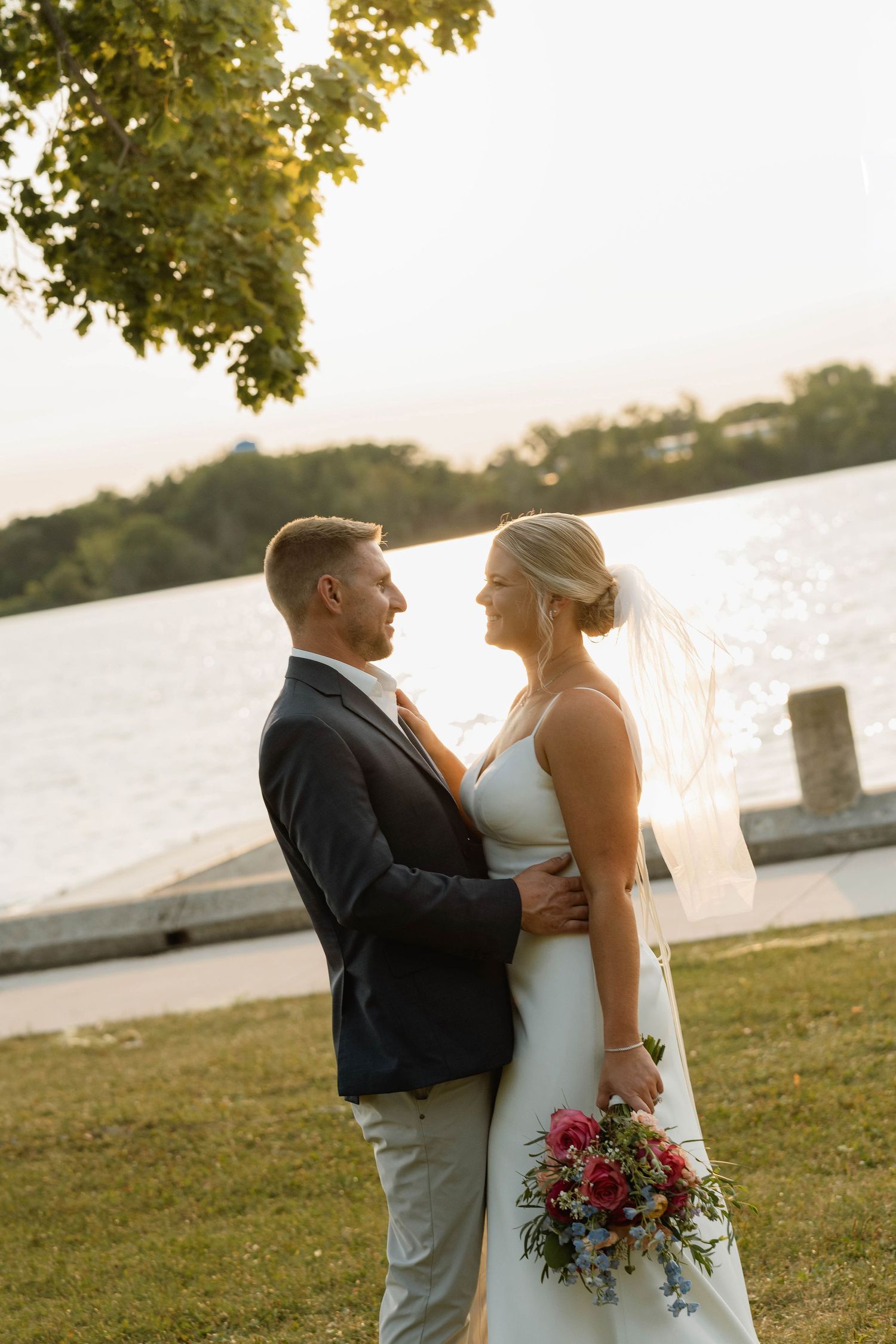 Bride and groom embracing near lakeside at golden hour sunset.