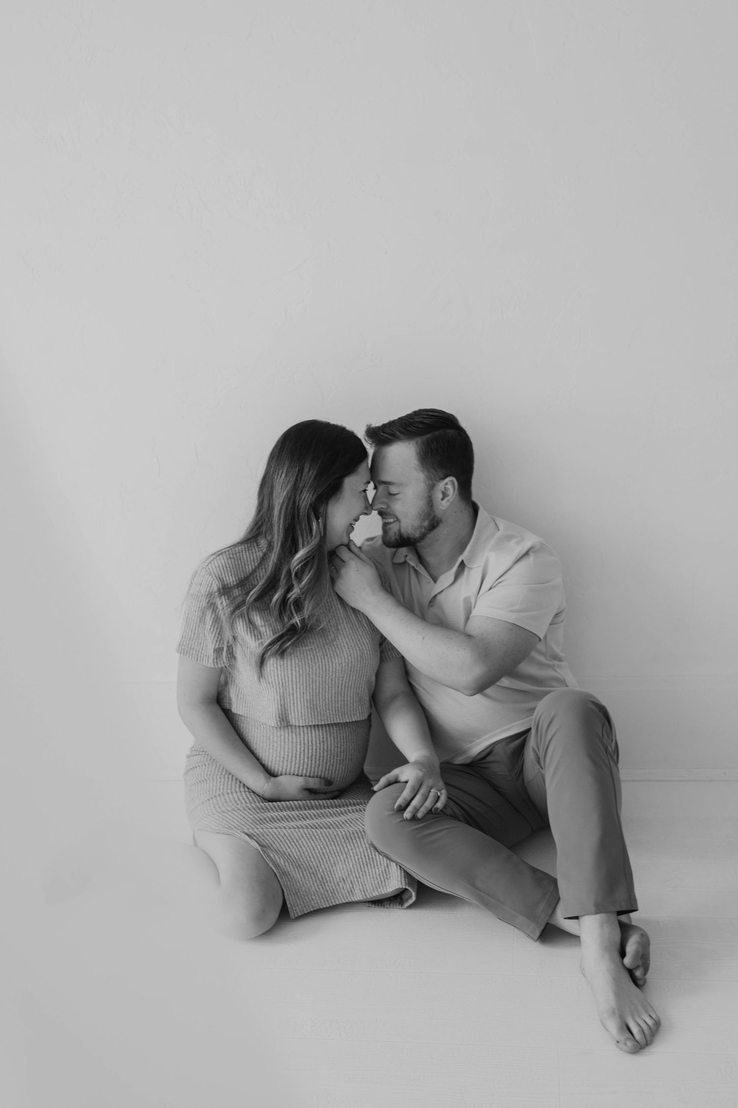 Black and white photo of couple kissing, pregnant woman cradling baby bump on floor.