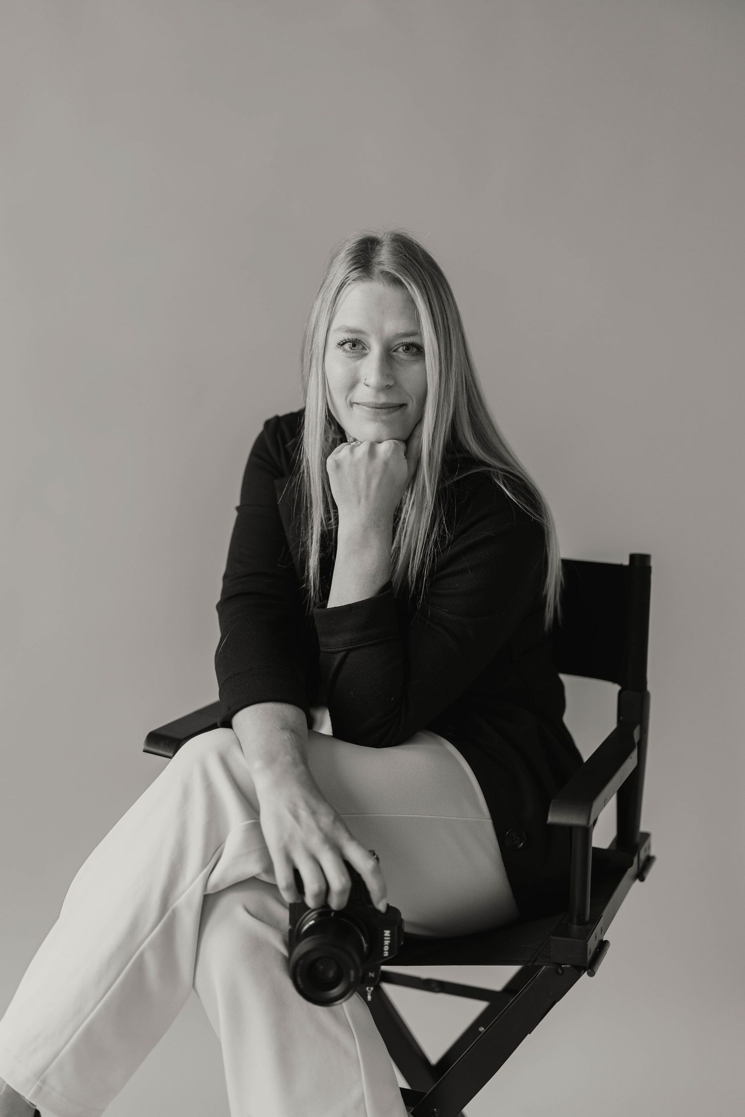 Black and white portrait of a smiling blonde female photographer posing in a director's chair.