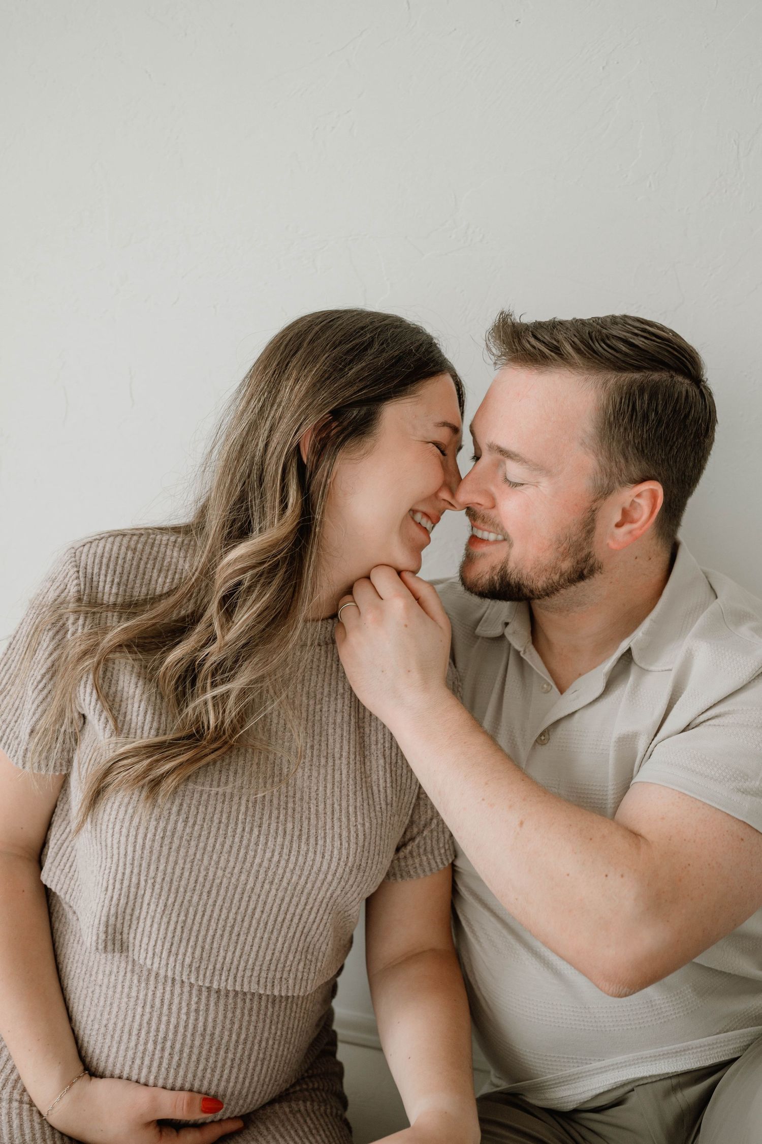 Happy couple nose-to-nose smiling, man gently holding pregnant woman's face close.