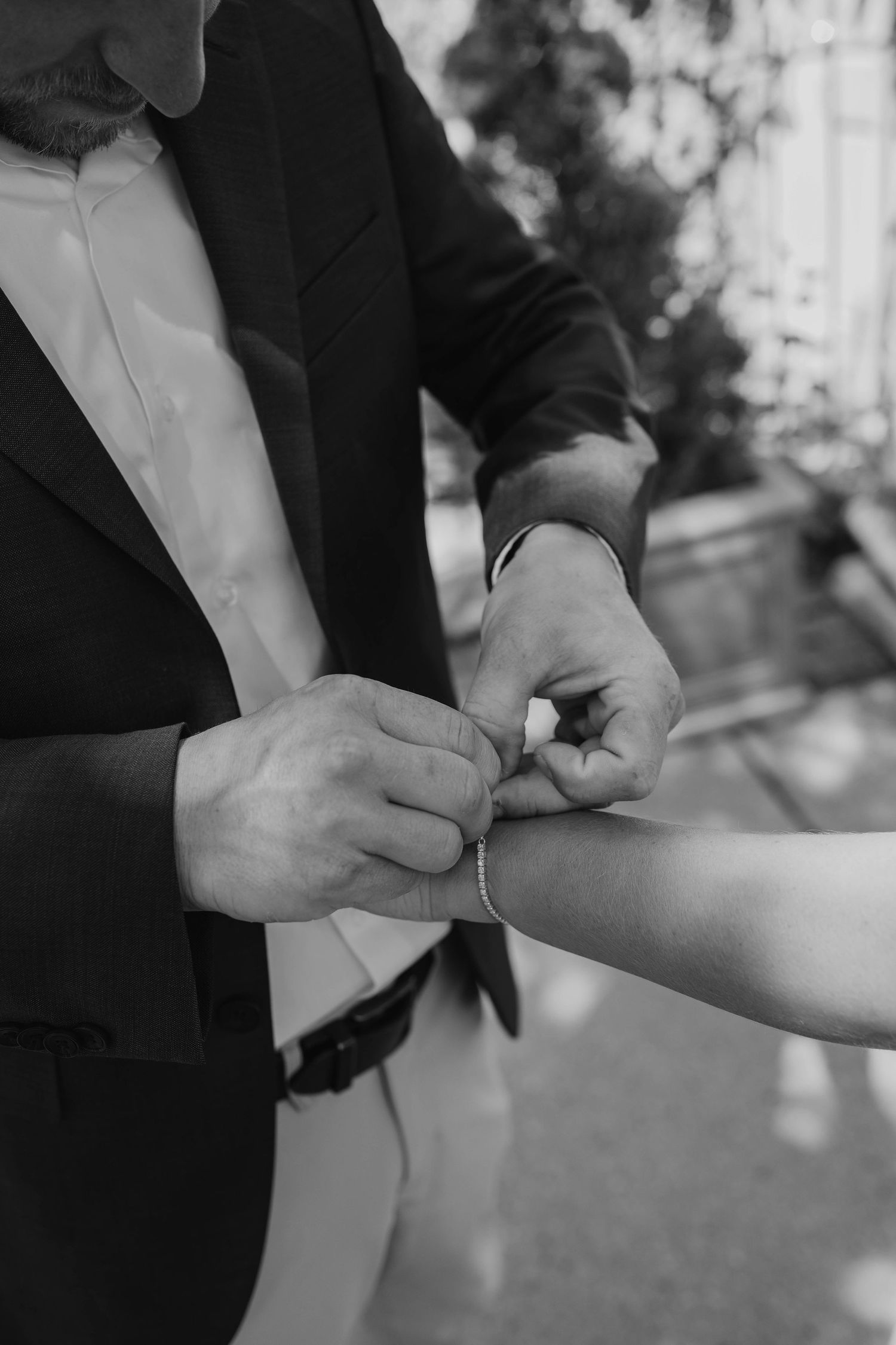 Black and white photo of groom fastening bracelet on bride's wrist.