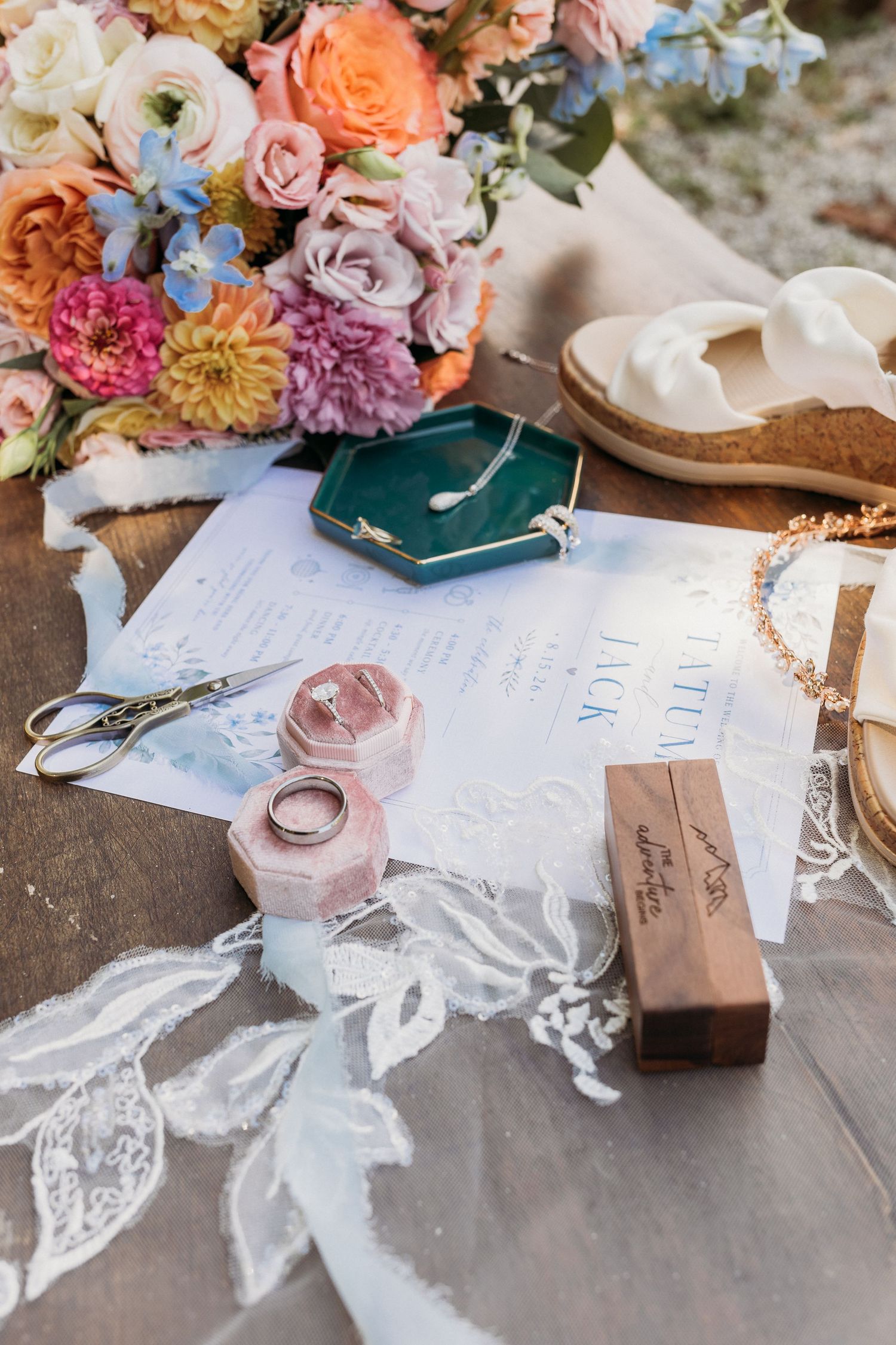 Colorful bridal bouquet beside wedding stationery, jewelry, pink ring boxes, and white bridal shoes.