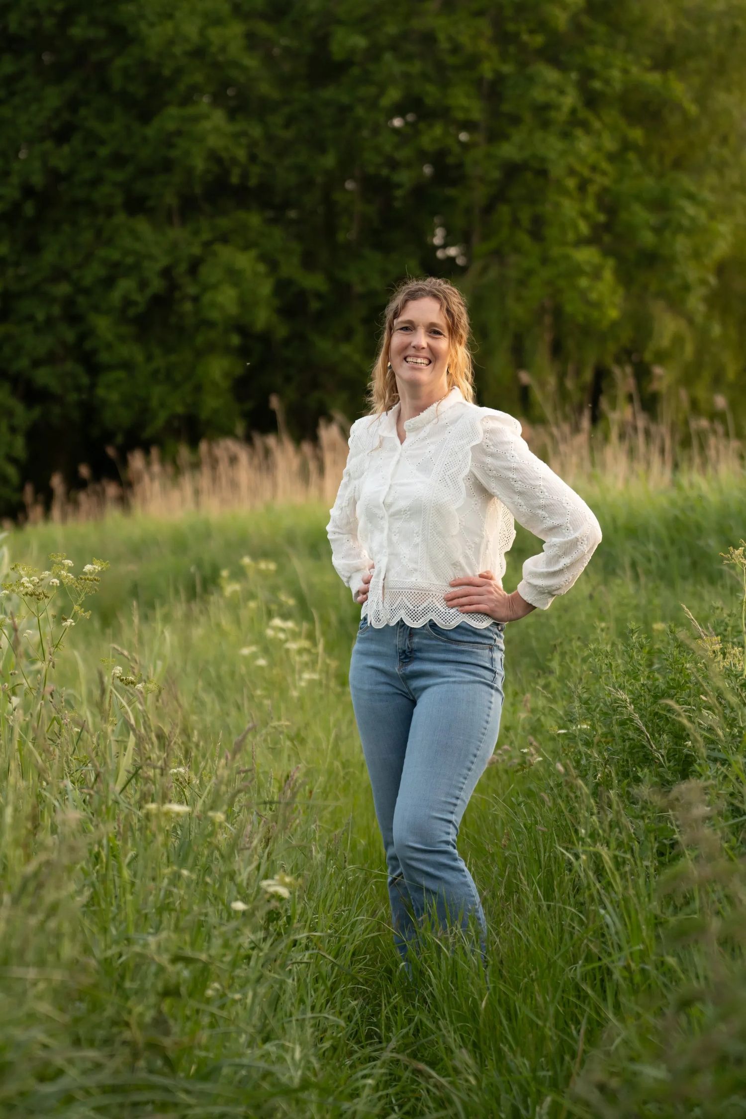 Person in white blouse and jeans standing in tall grass during golden hour.