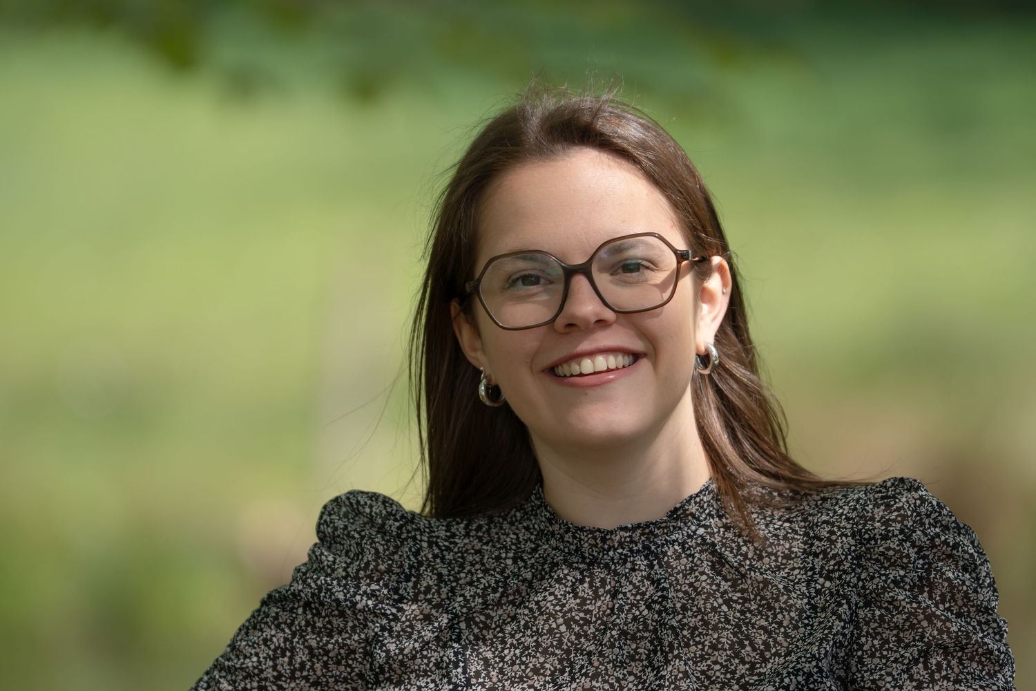 een knap donkerharig meisje met een bril aan poseert in een natuurdomein