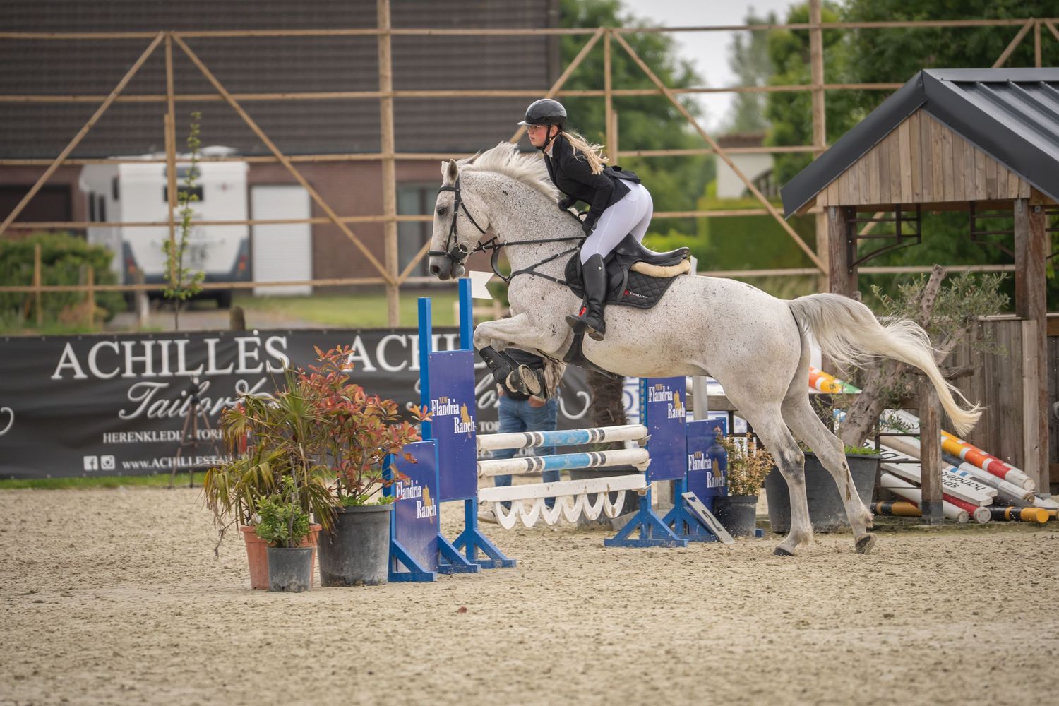 White horse and rider clearing high fence during equestrian show jumping competition.