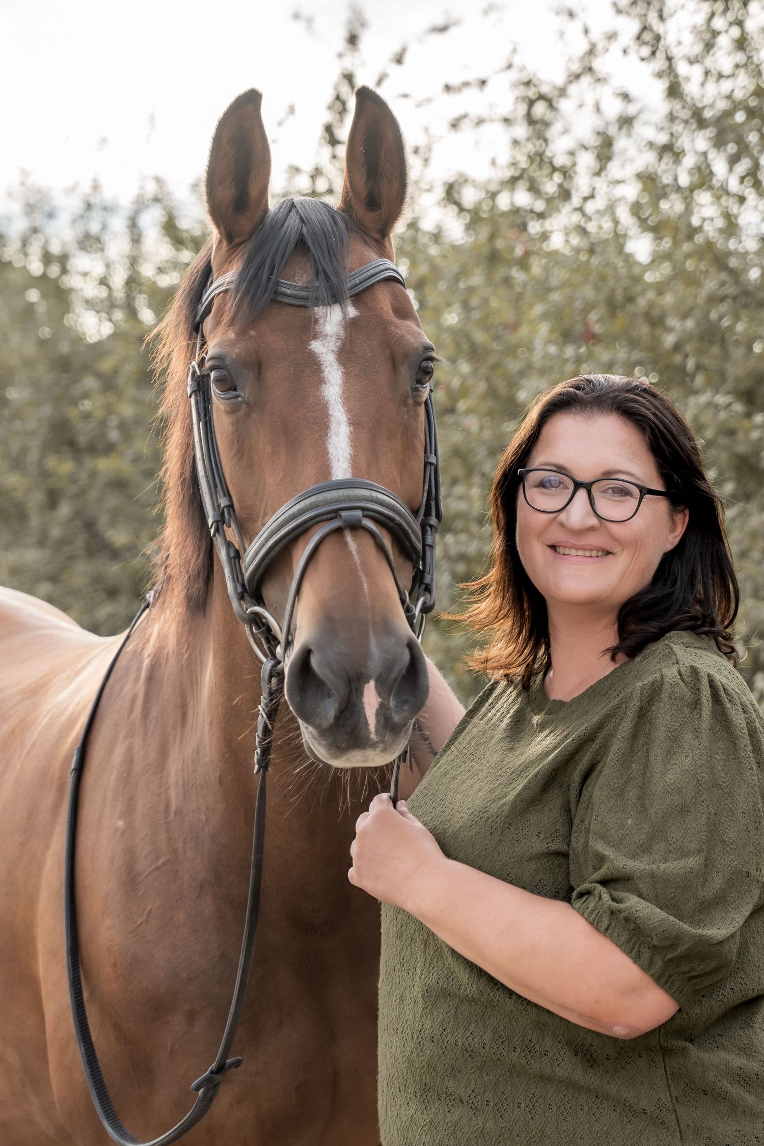 A beautiful brown horse stands close to someone wearing an olive green shirt in an outdoor setting.