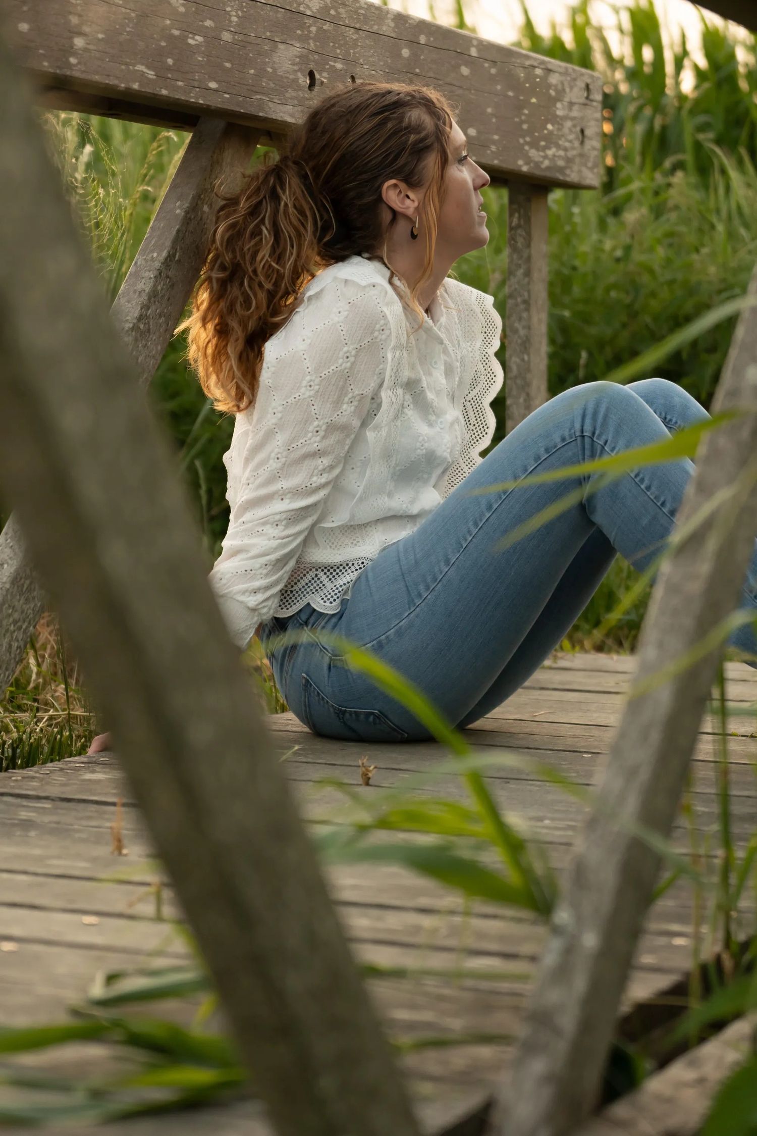 Person in white blouse sitting on wooden deck surrounded by natural vegetation.