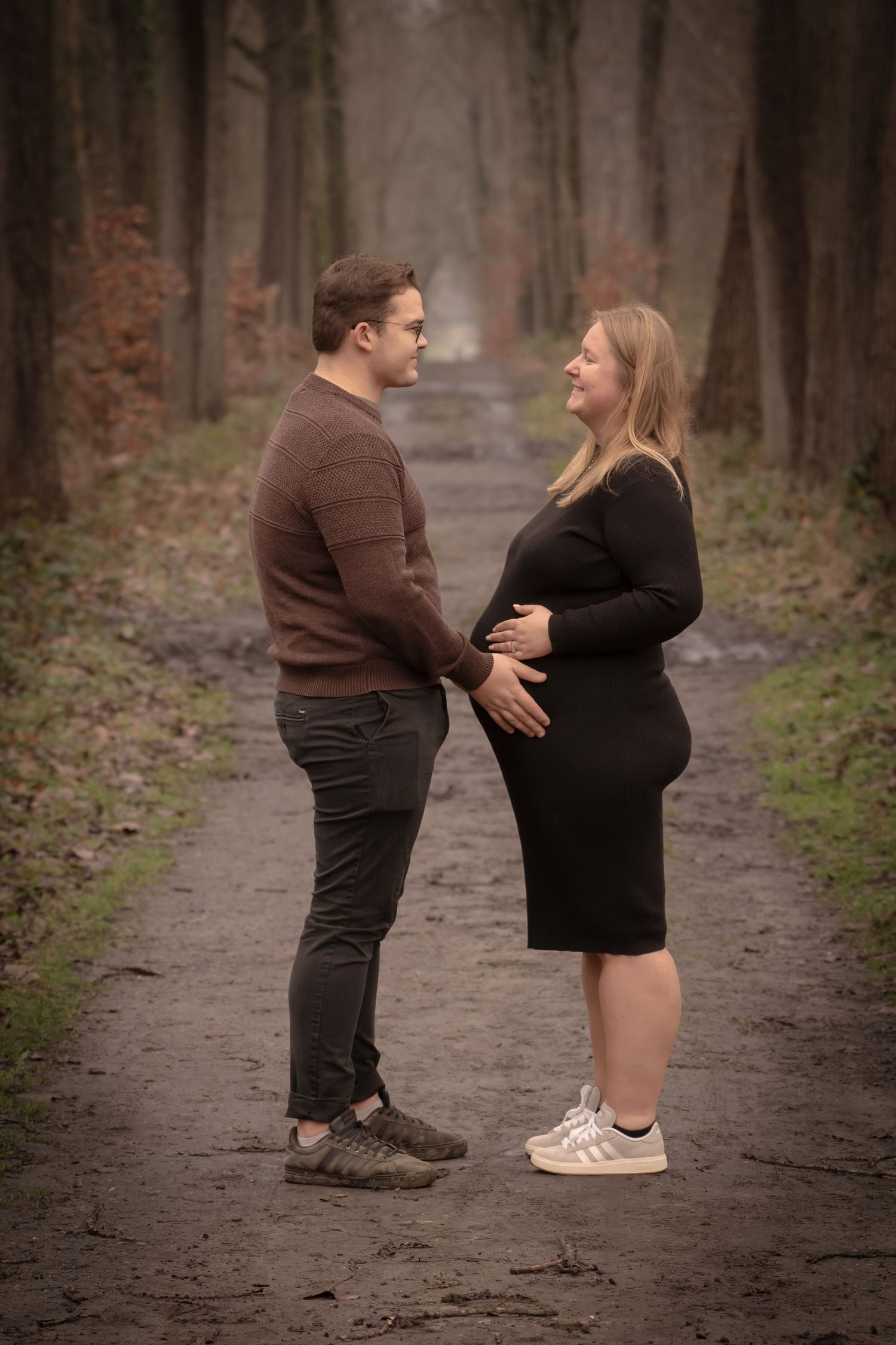 A couple in casual attire shares a romantic moment on a misty forest path during an autumn day.