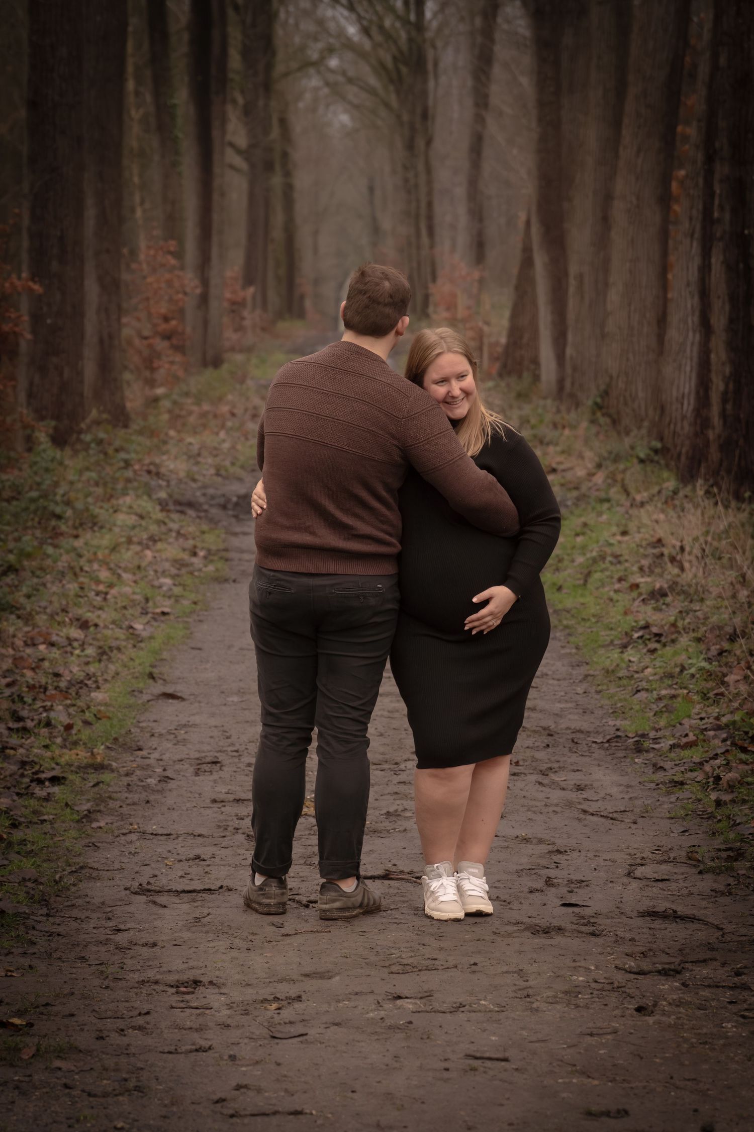 A couple in dark clothing walking together down a wooded path in autumn.