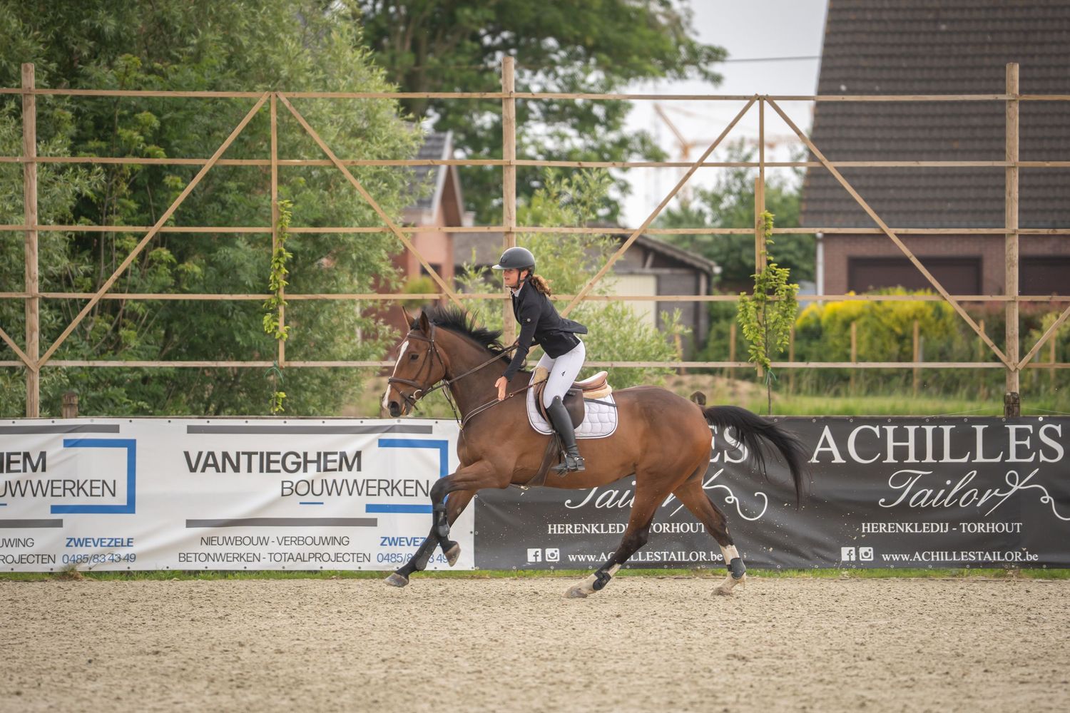Show jumper performing dressage routine in competition arena with sponsorship banners.