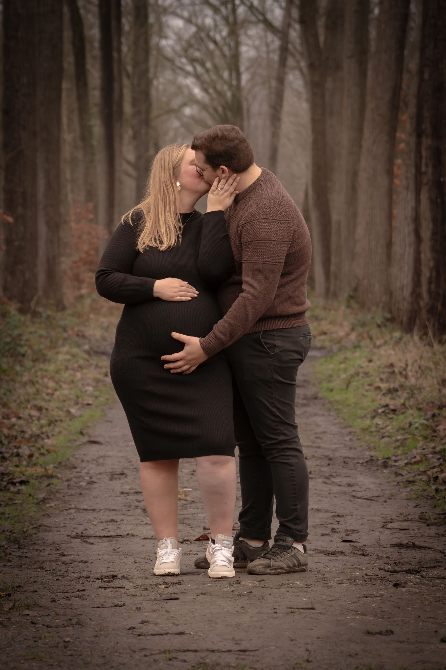 A couple shares a romantic moment while walking along a wooded path in autumn.