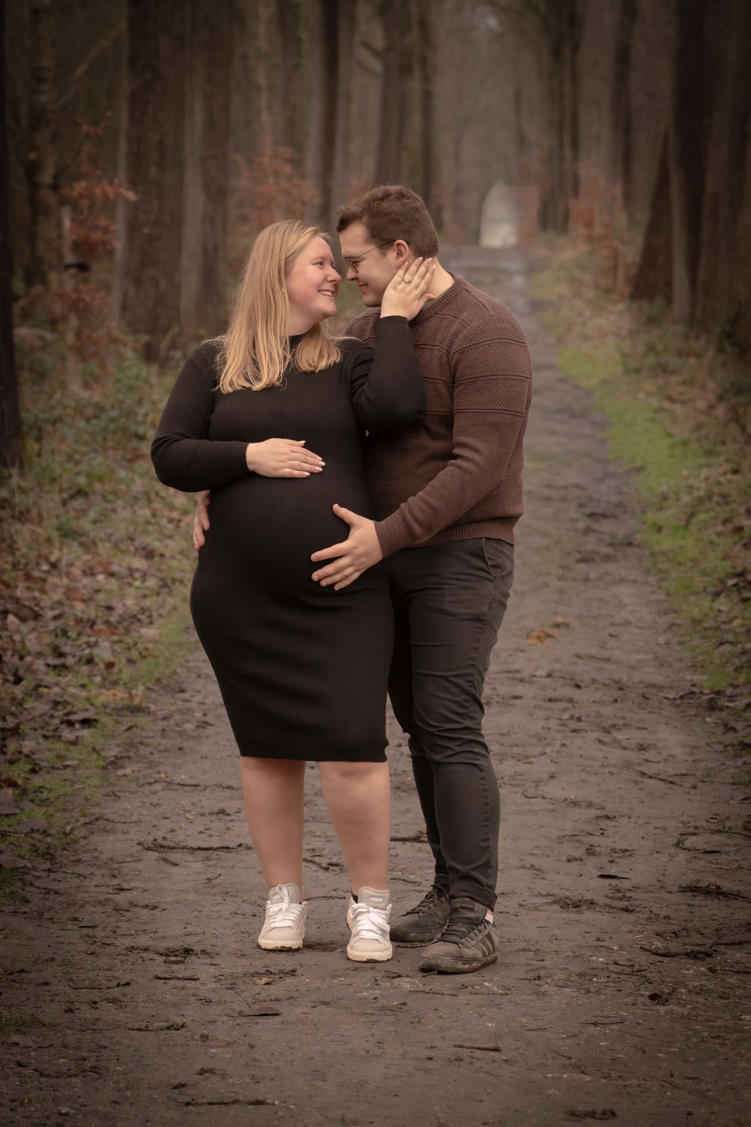 A couple shares an intimate moment on a forest path as they await their new arrival.