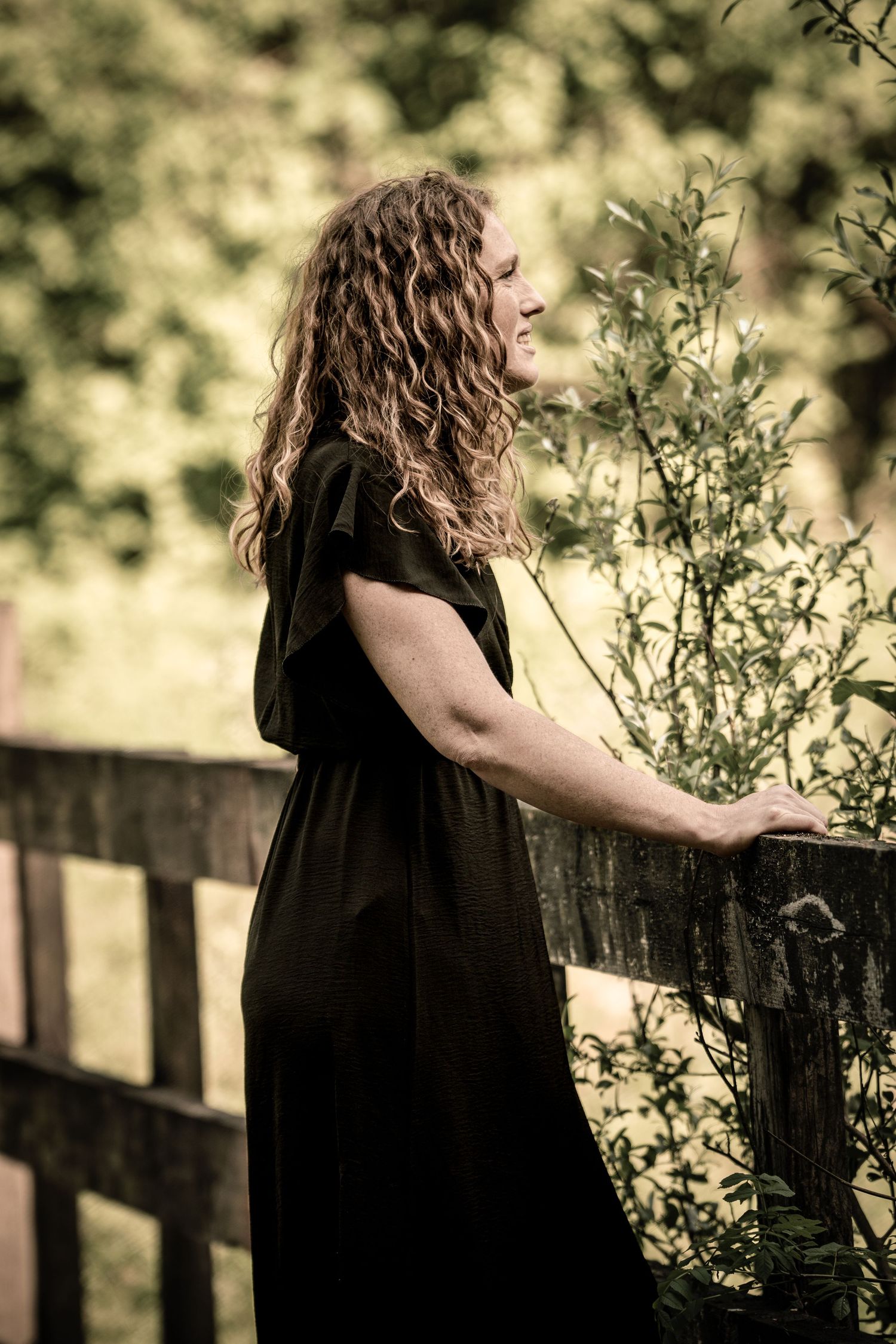 Side view of person in black dress standing on wooden bridge in natural setting.