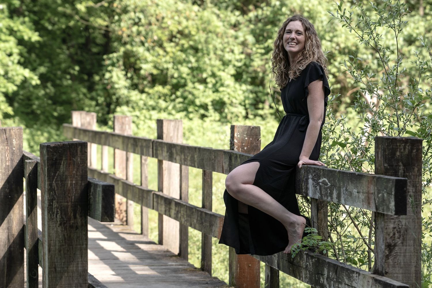 Person posing artistically on wooden fence posts in summer garden setting.